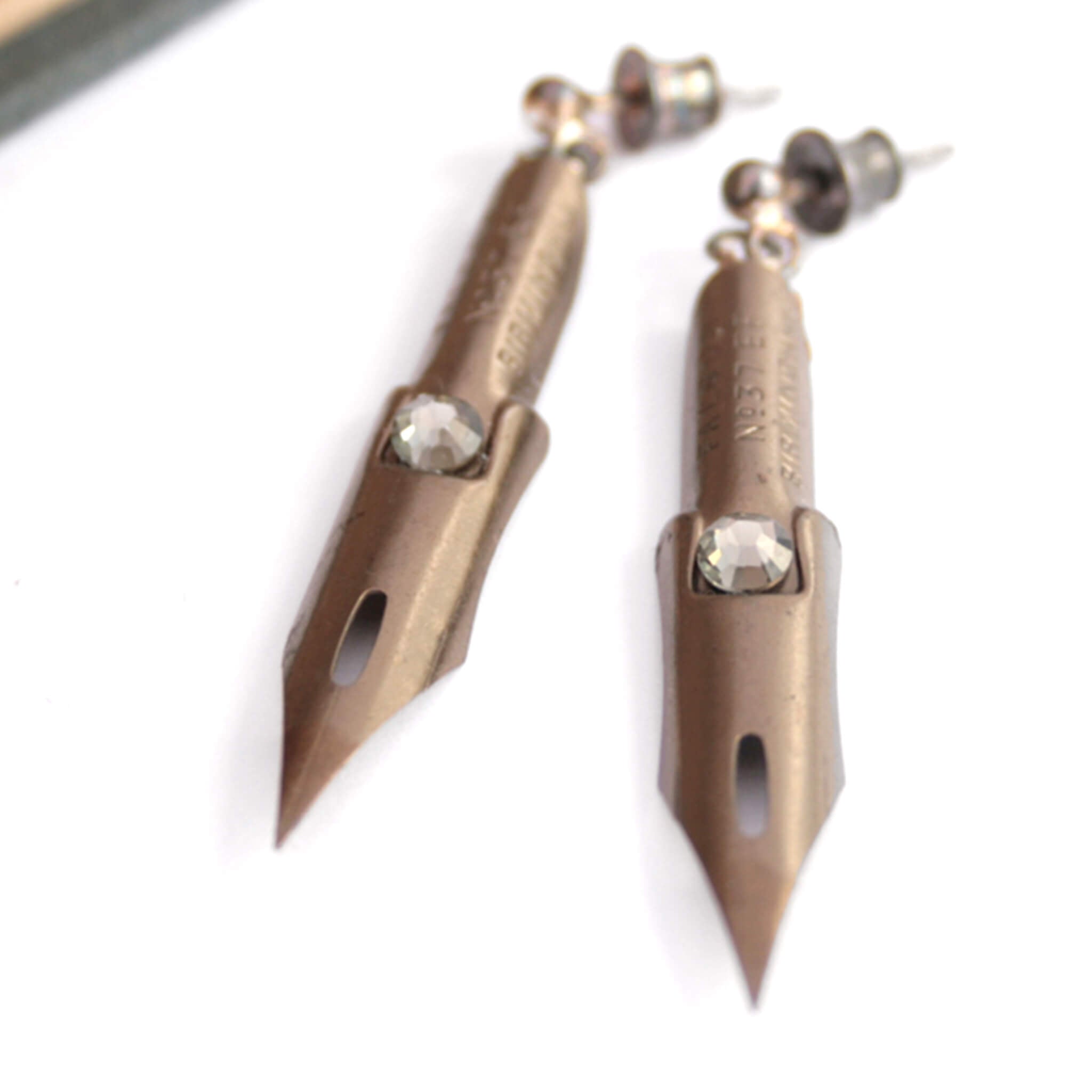 dark academia earrings made of pen nibs in bronze colour lying on a piece of white paper