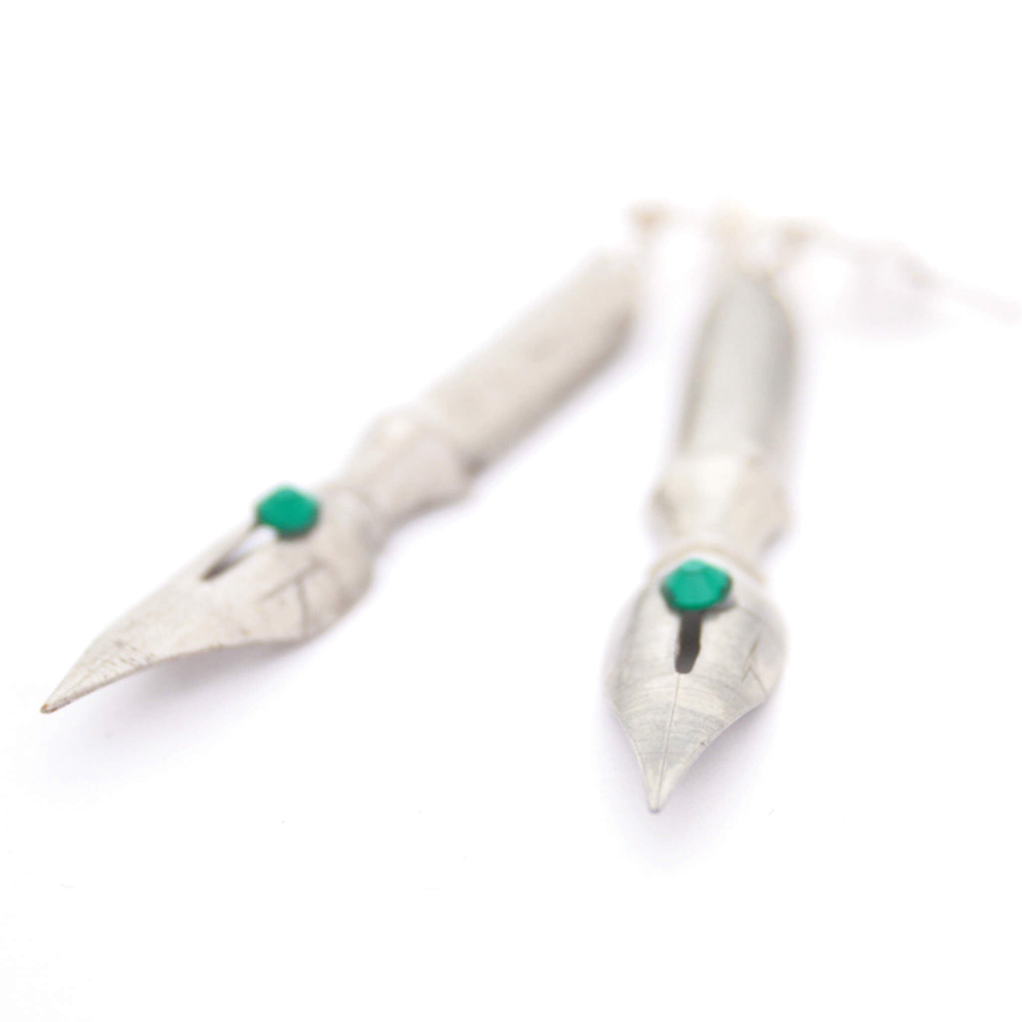 pen nib earrings with emerald birthstone crystals on them lying on a white paper