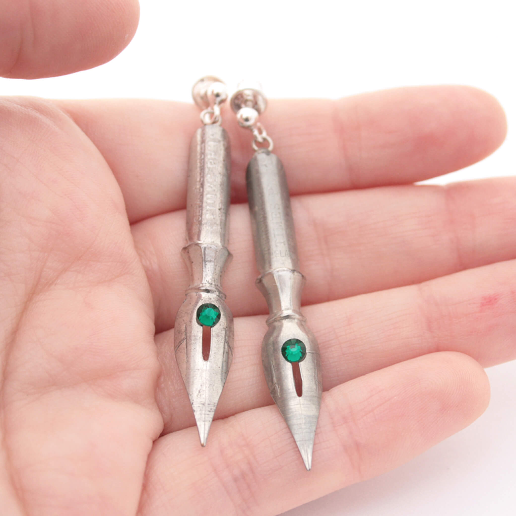 pen nib earrings with emerald birthstone crystals on them being hold in hand