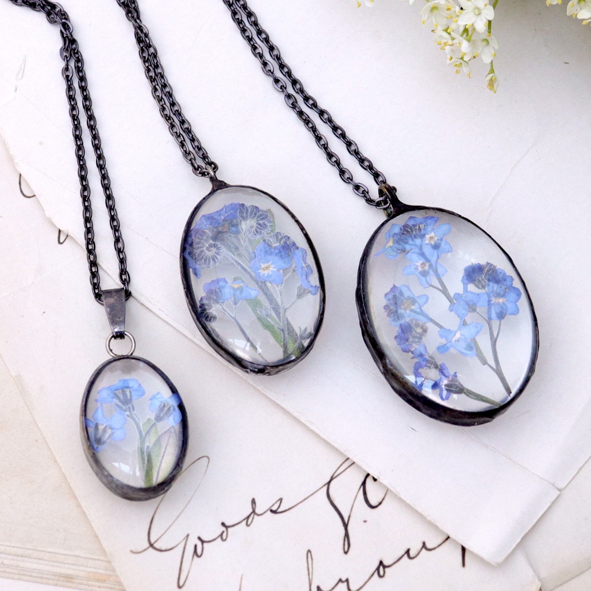 Three oval Forget-me-not necklaces lying on an old book side by side