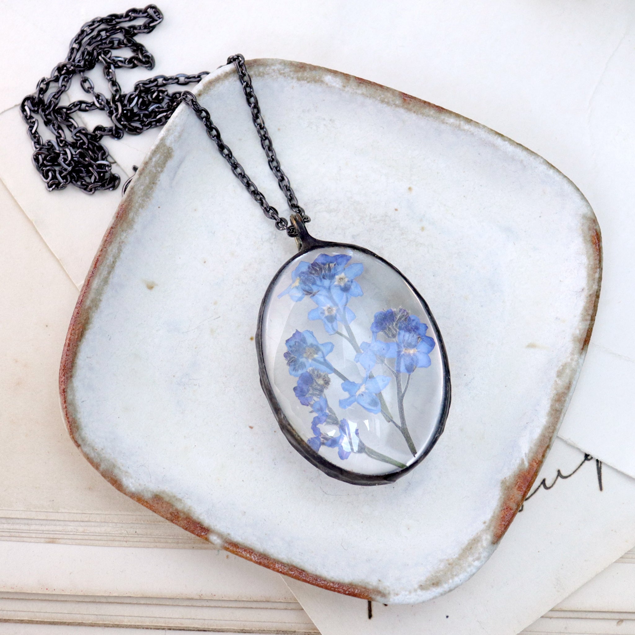 oval Forget-me-not necklace lying on a white dish