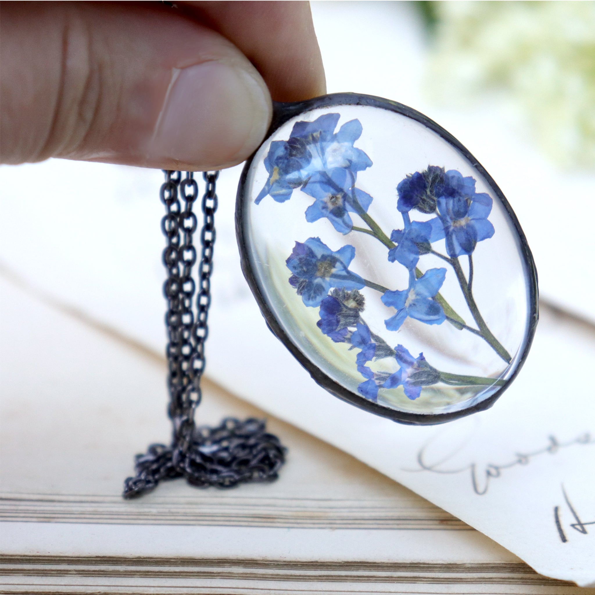 Forget-me-not oval shaped necklace being hold between thumb and index