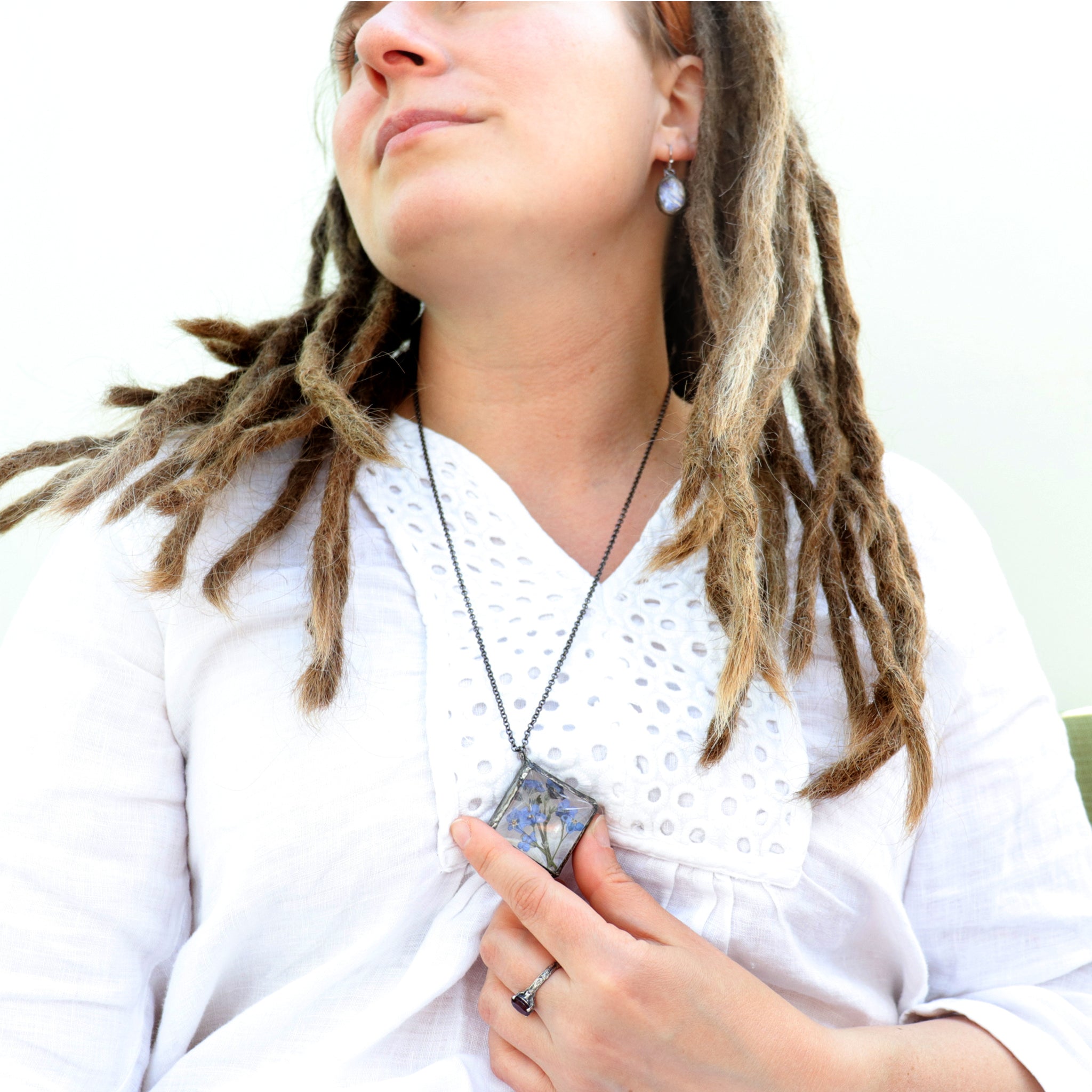 woman with dreadlock in a white blouse wearing and holding a diamond shaped necklace in her hand