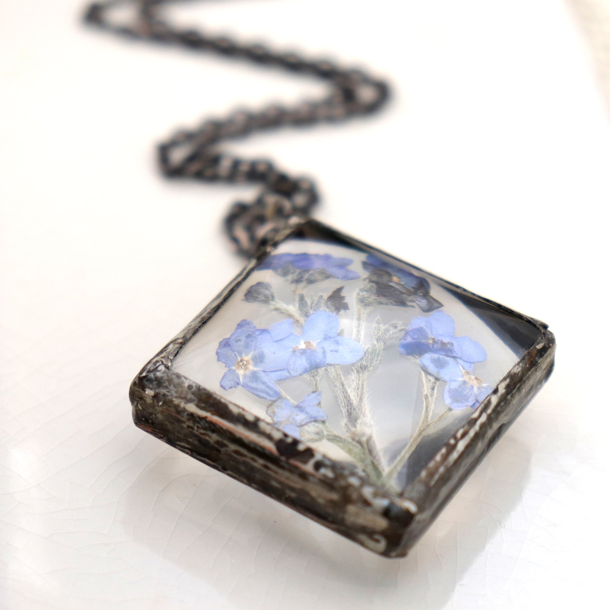 diamond shaped Forget-me-not necklace lying on a white dish