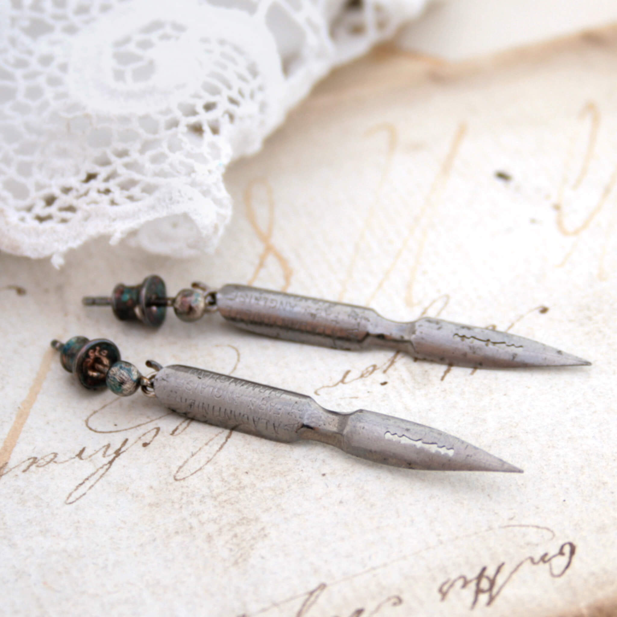 quirky earrings made of antique pen nibs lying on an old letter