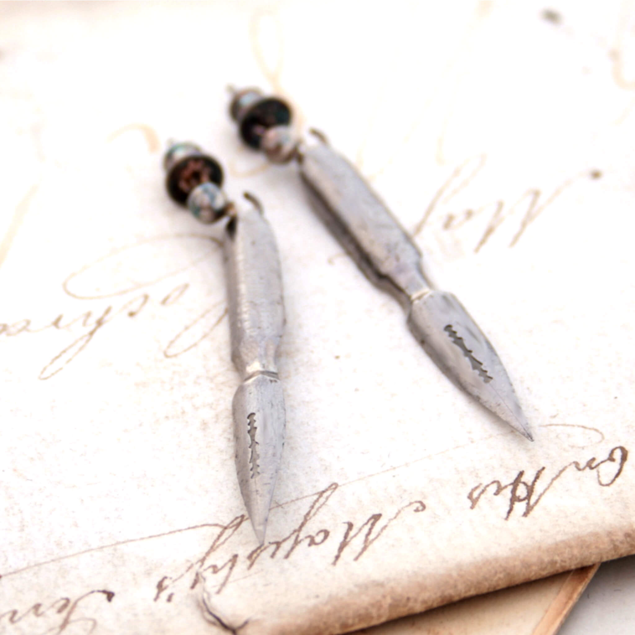 quirky earrings made of antique pen nibs lying on an old letter