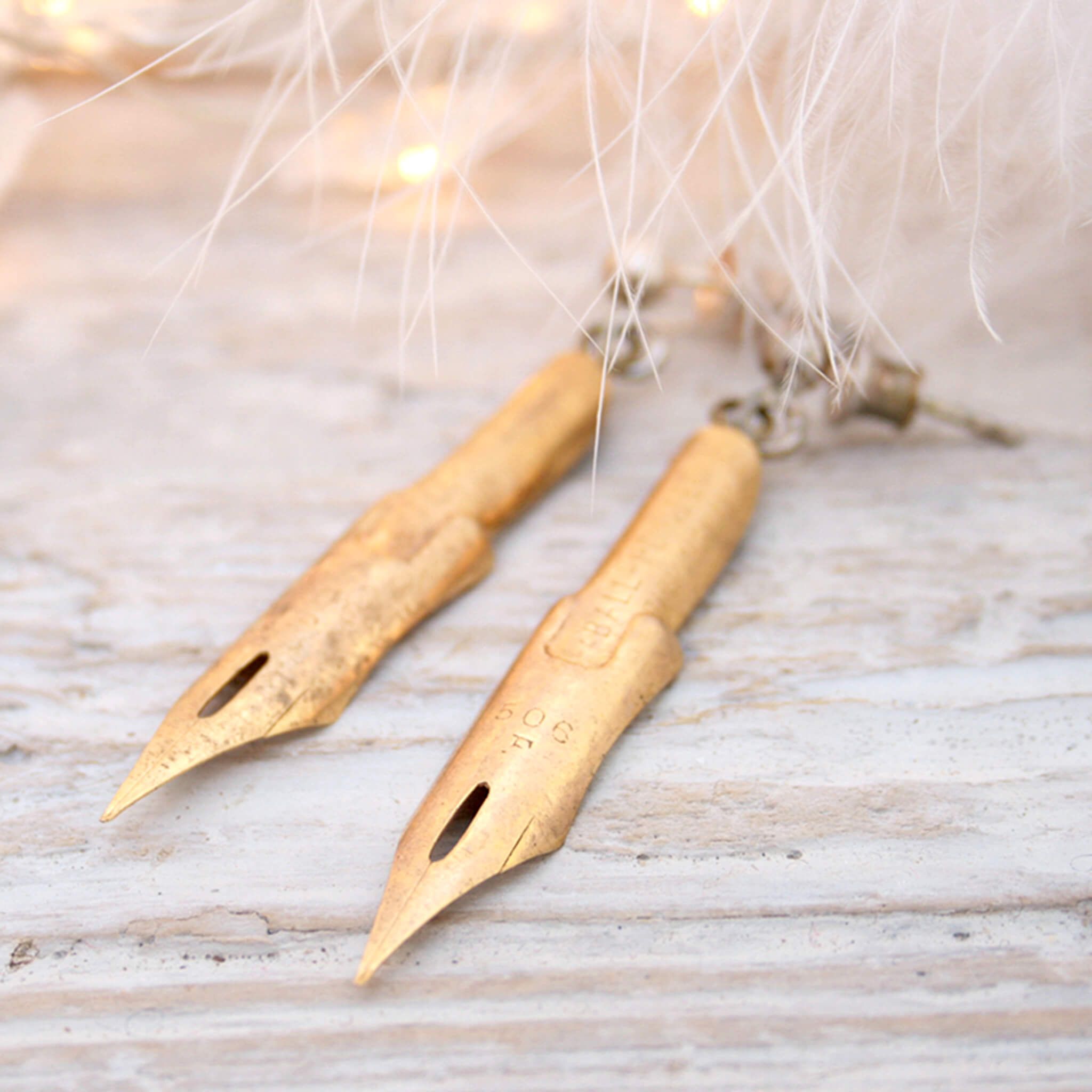 dark academia earrings made of gold coated pen nibs lying on a white piece of wood