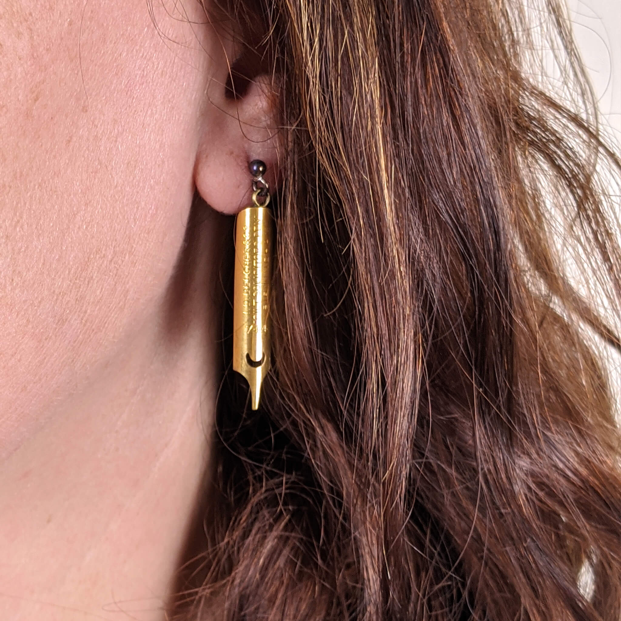 brunette woman wearing gold coated pen nib earrings