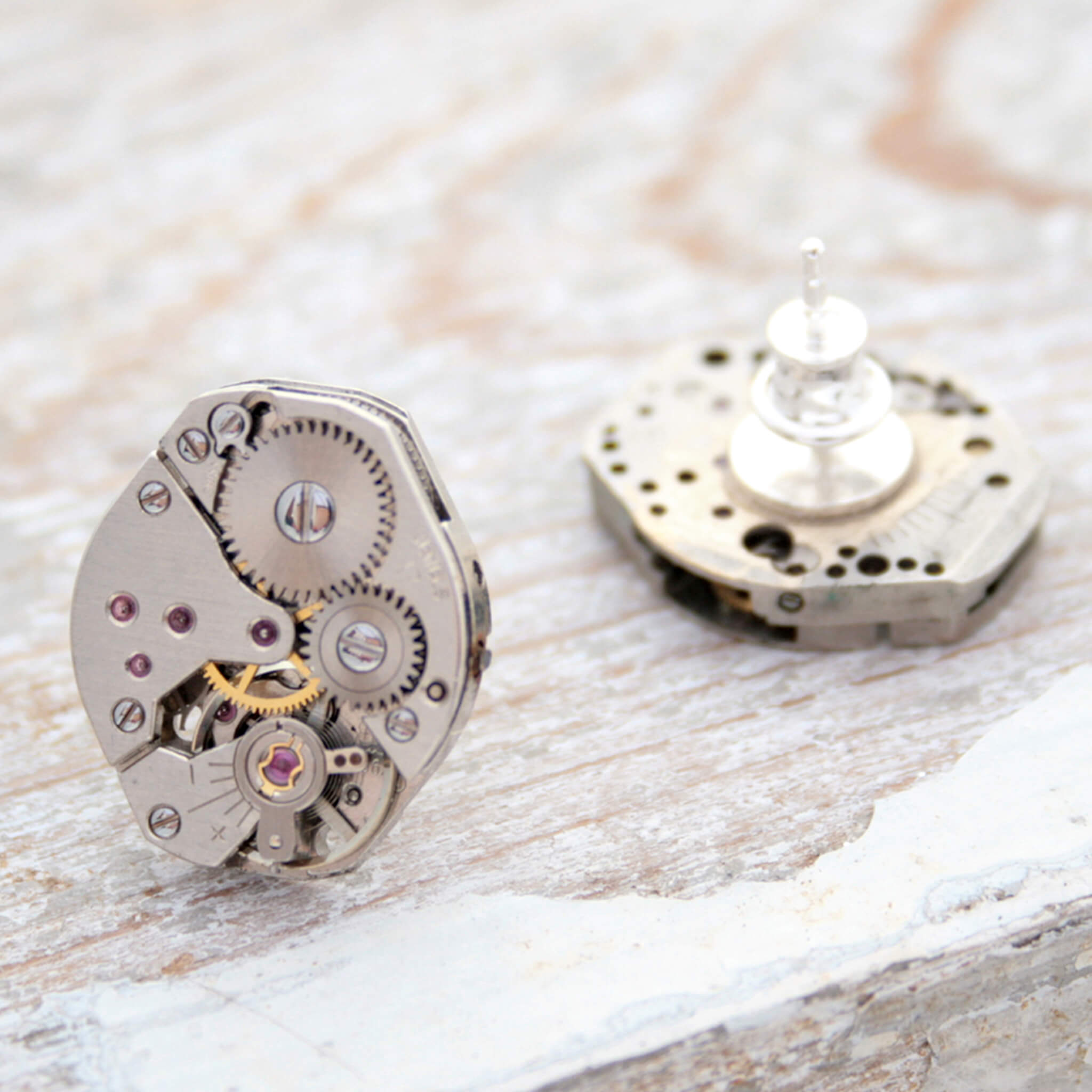 watch movements turned into stud earrings lying on a white painted wood
