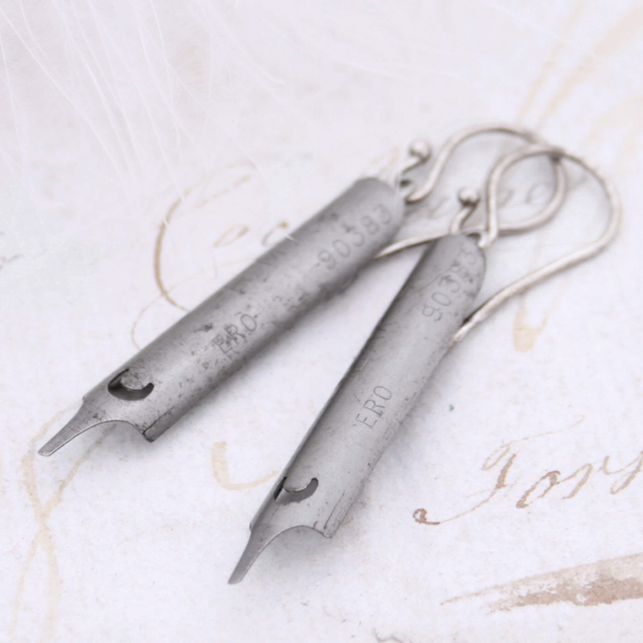 steel pen nib earrings lying on an old letter