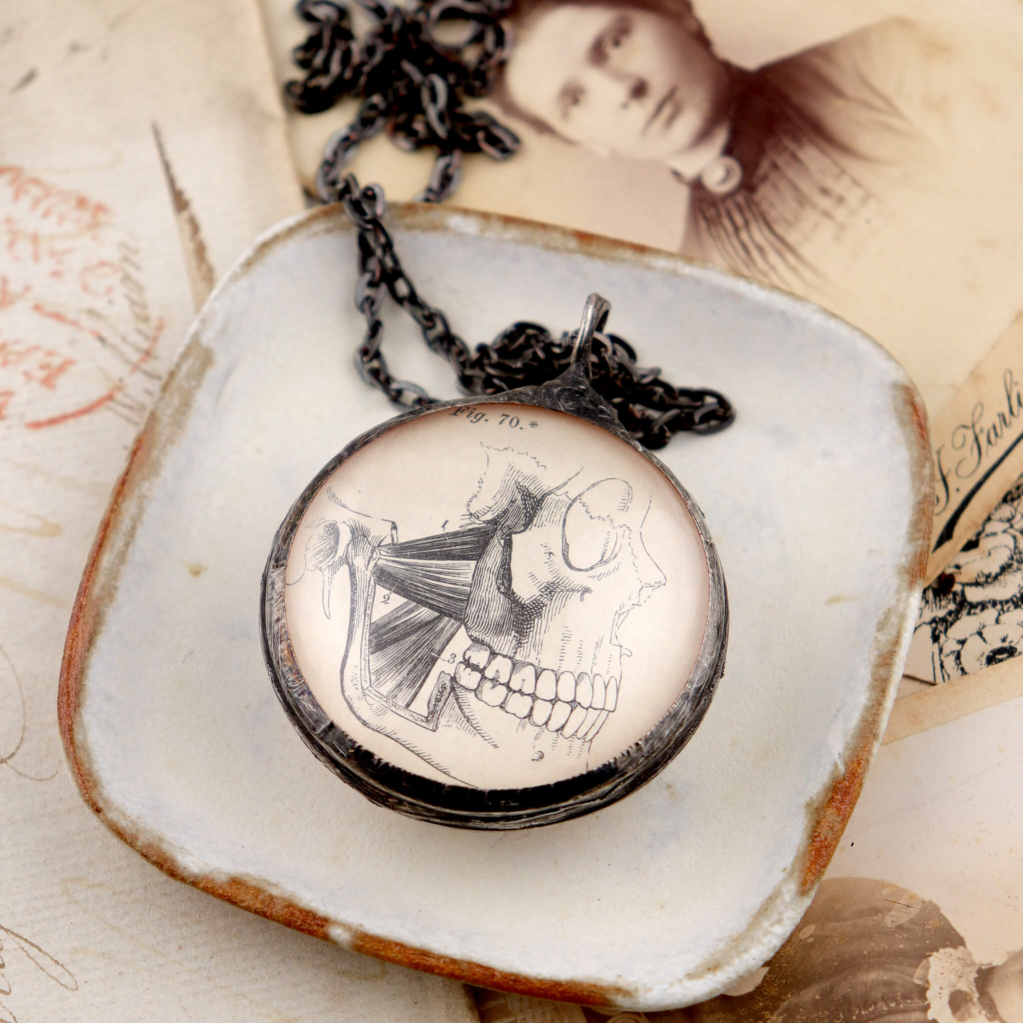 dark academia skull illustration necklace lying on piece of pottery and antique portrait