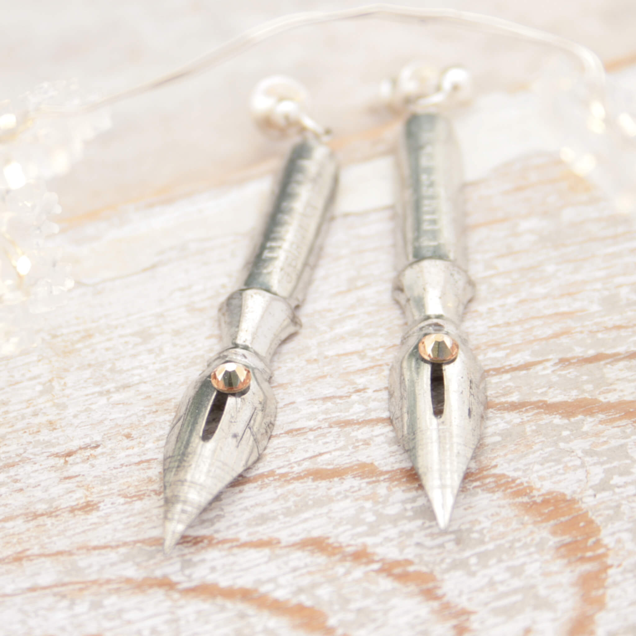 pen nib earrings with light topaz crystals on them lying on a white wooden plank