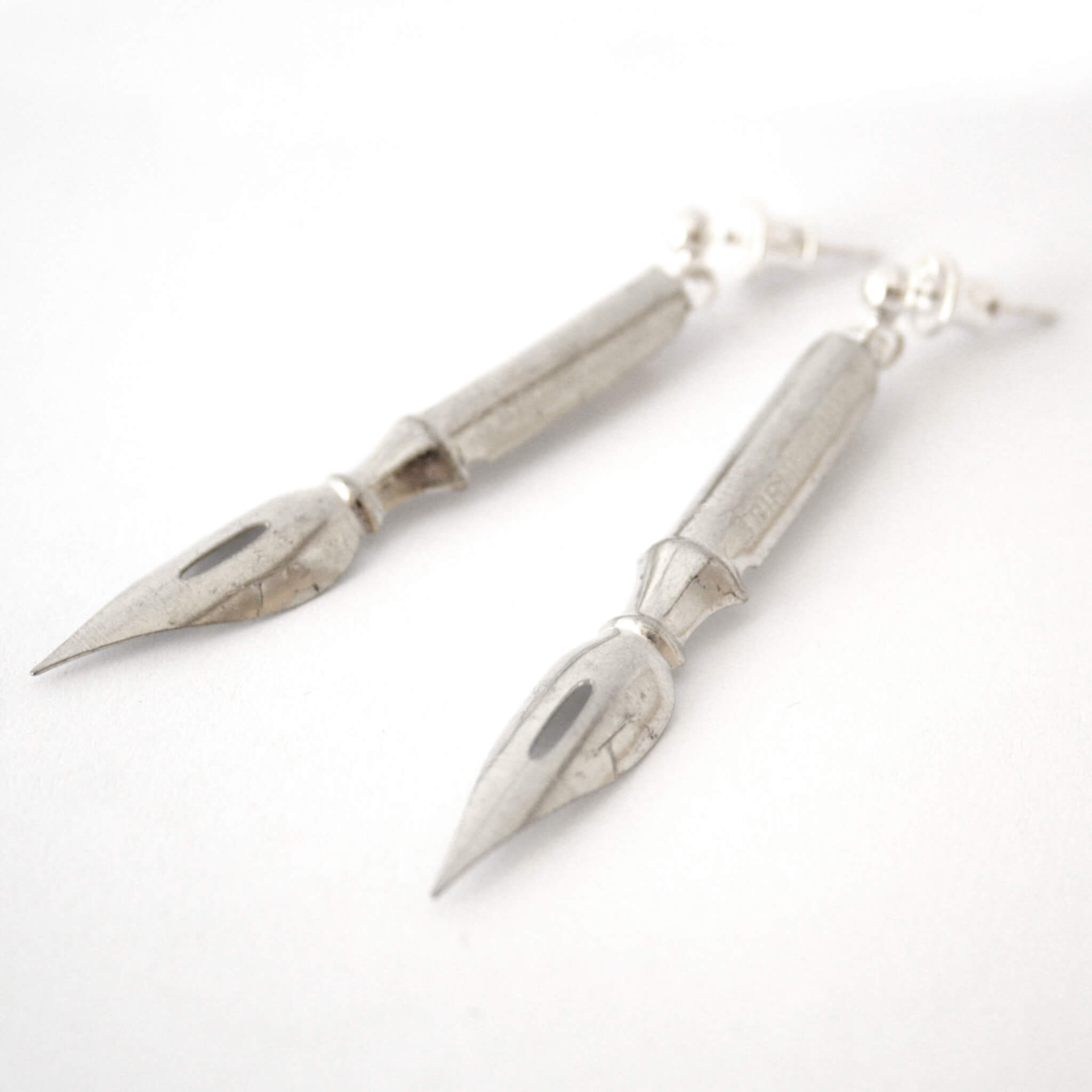 silver tone pen nib earrings lying on a piece of paper