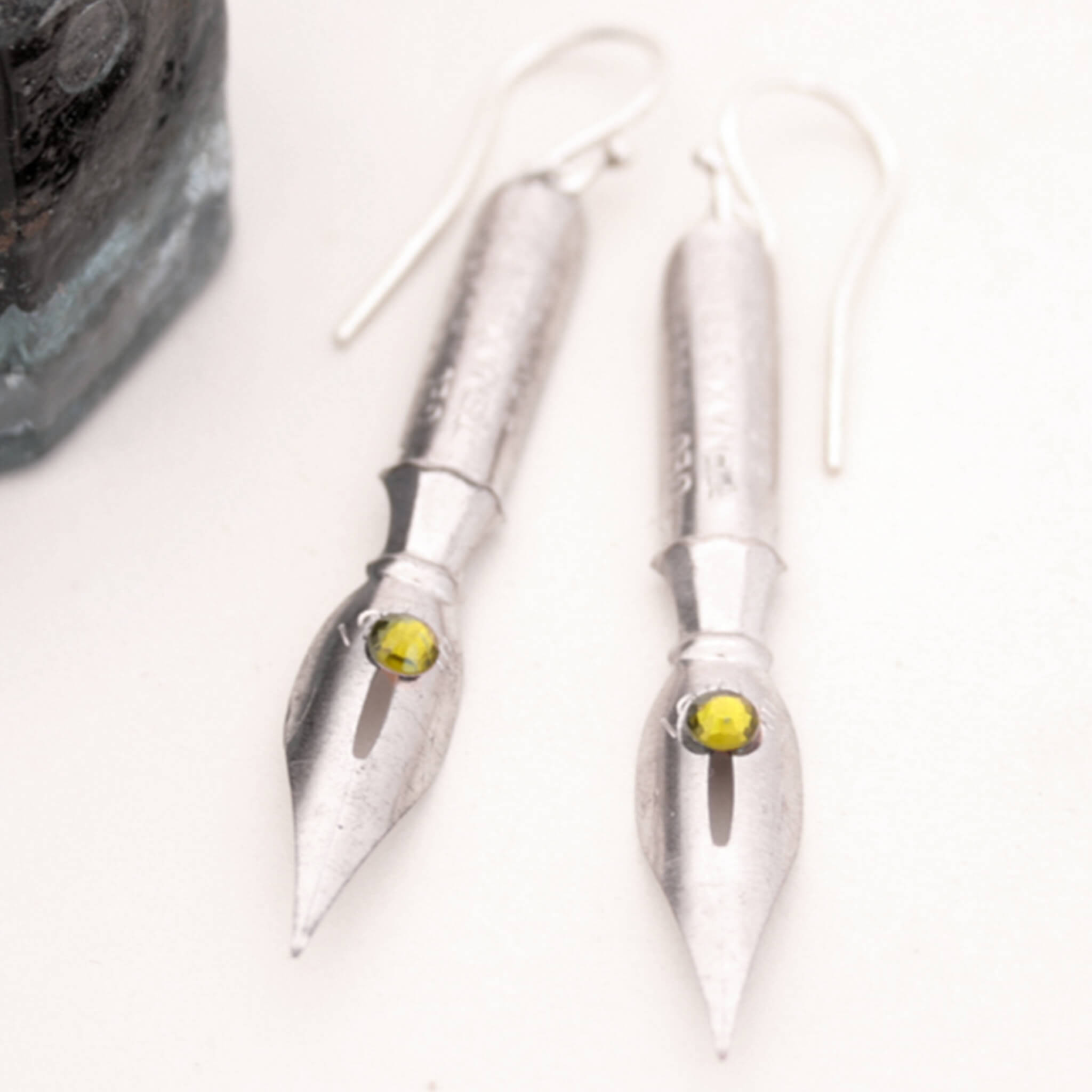 pen nib earrings with olivine crystals on them lying on a piece of paper