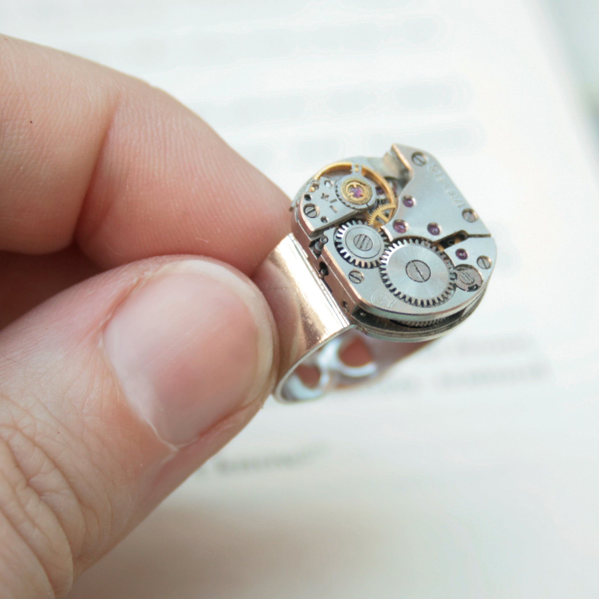 Mens Pinky Ring in Steampunk Style made of watch movement in silver color being hold in hand