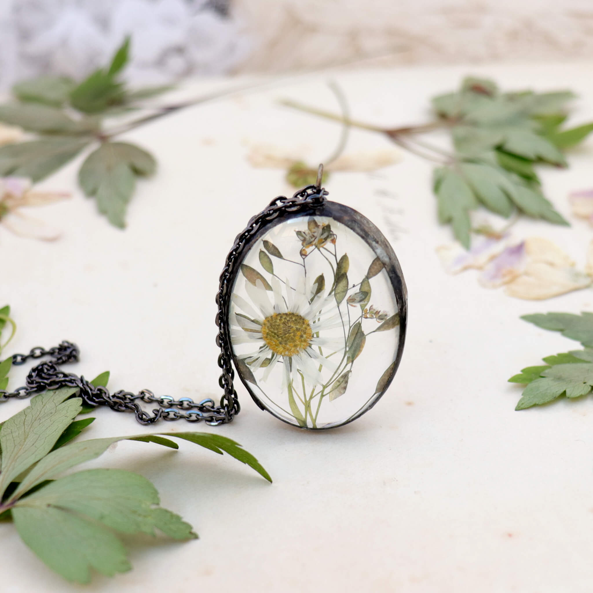 Pressed daisy necklace in oval shape standing on an edge on an old paper. Pressed anemones around