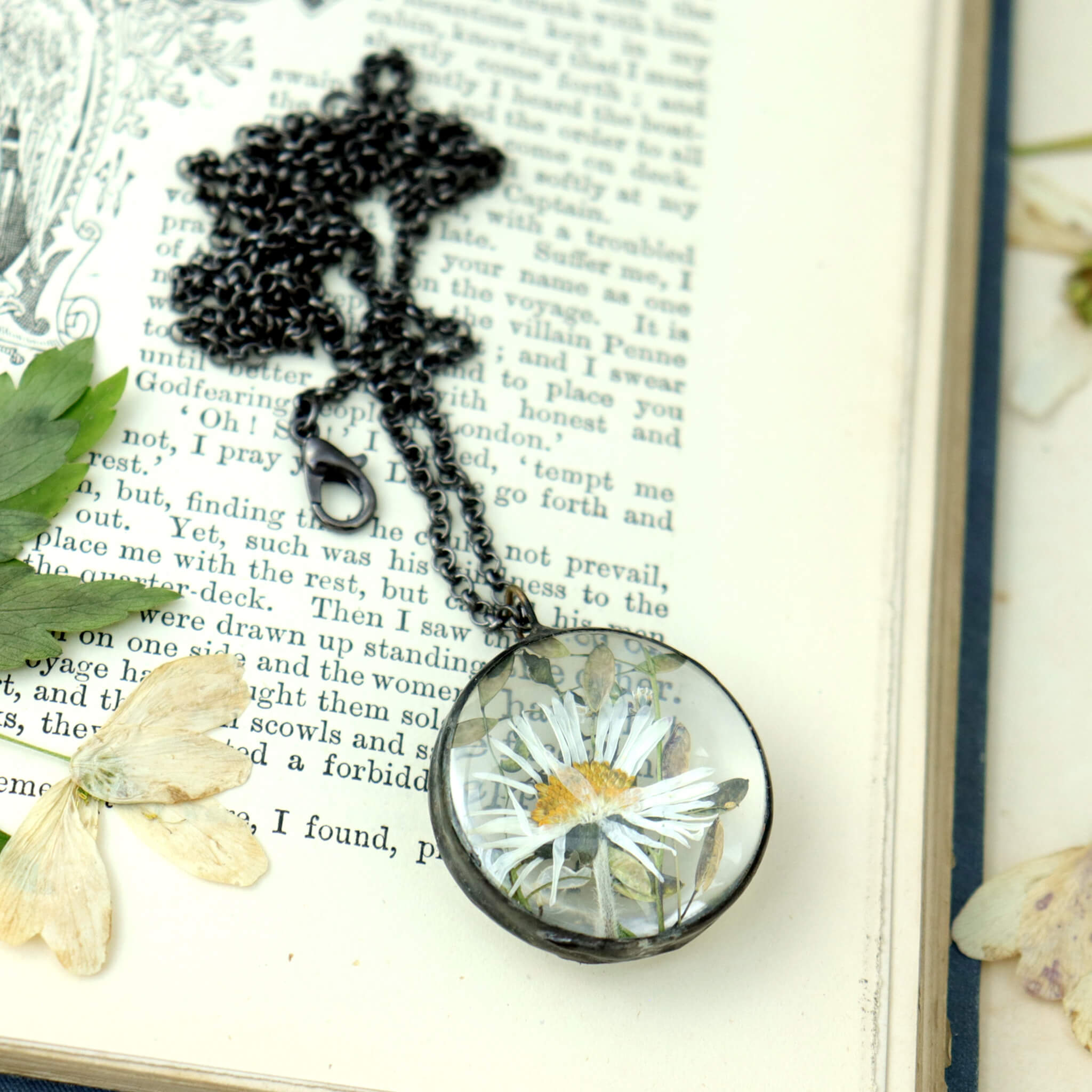 Pressed daisy necklace in round shape lying on an old book. Pressed anemones around