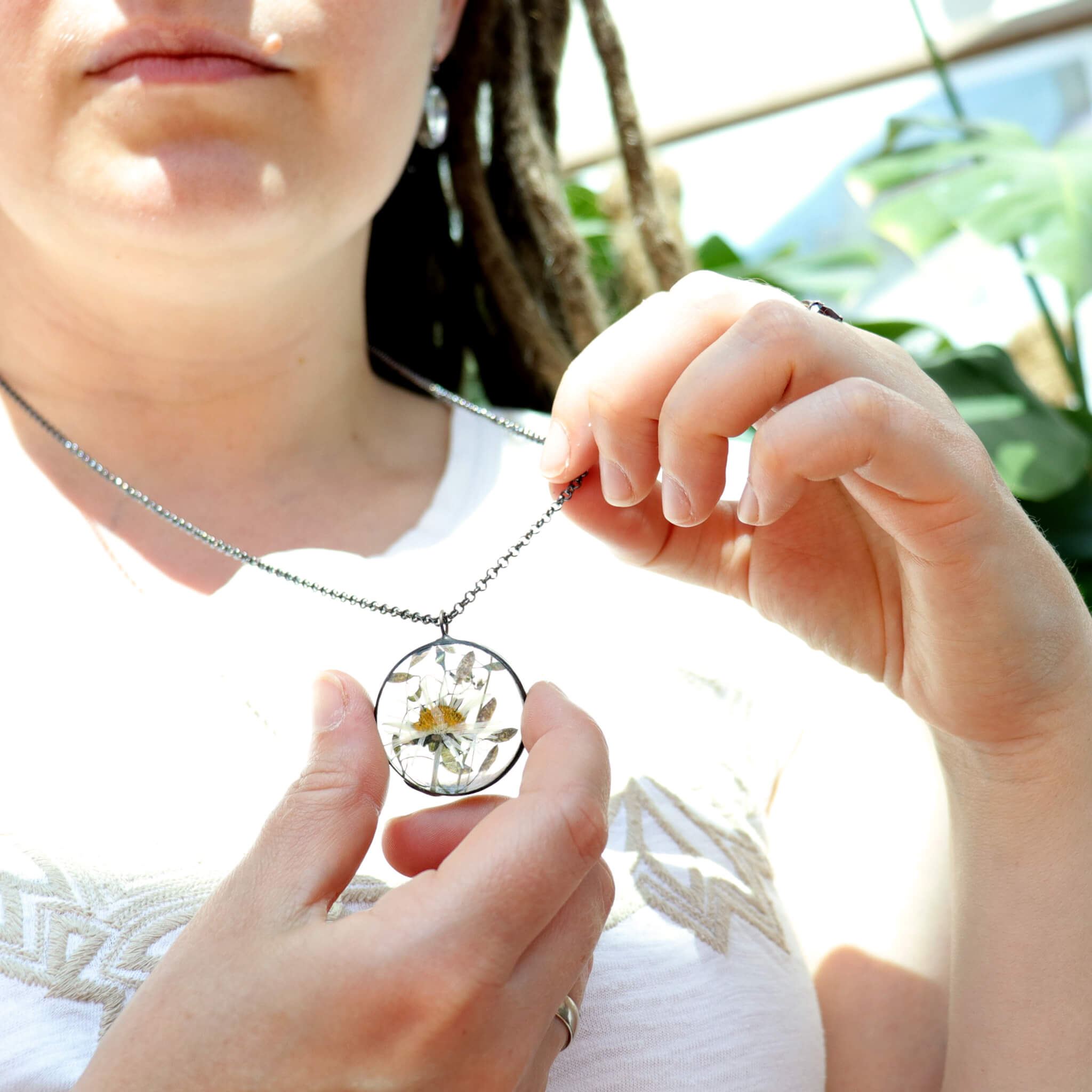 Lady in white blouse holding Pressed daisy necklace in round shape in hands 