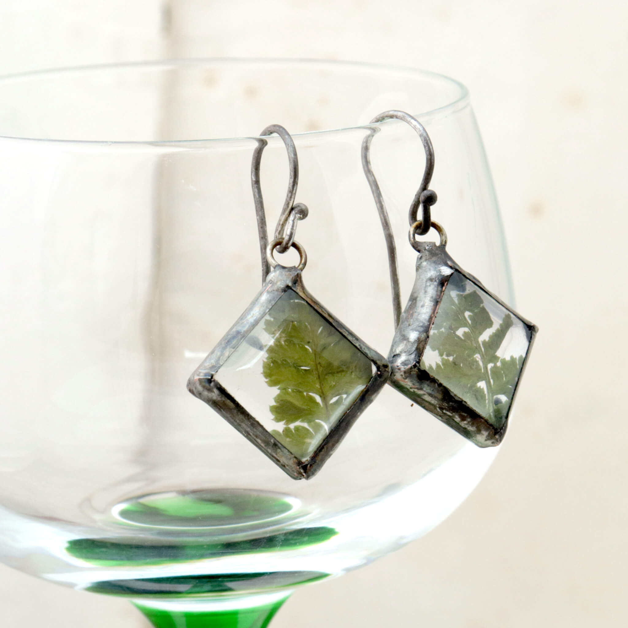 Earrings with real fern hanging on an edge of wine glass