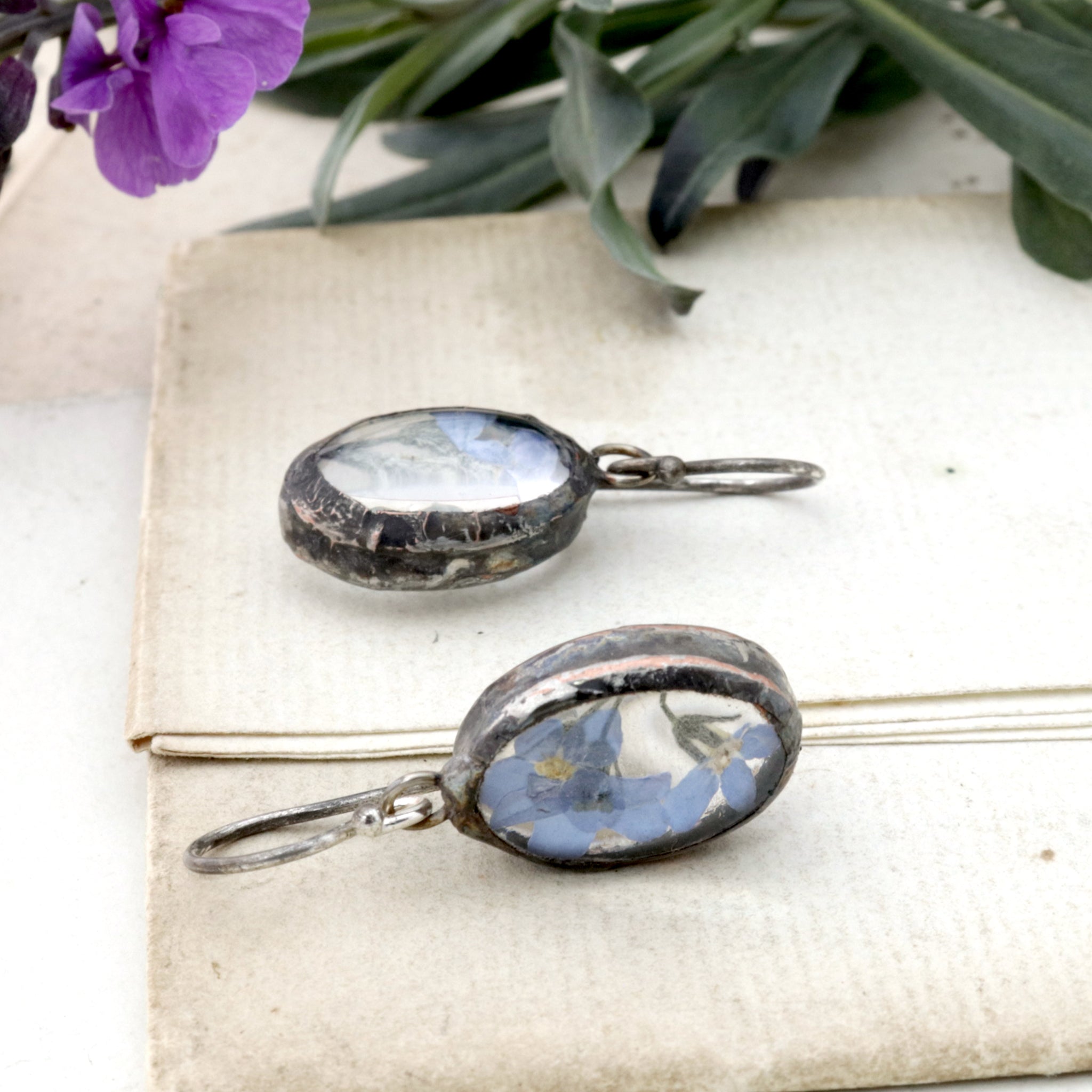 Oval forget-me-not earrings lying on an old letter