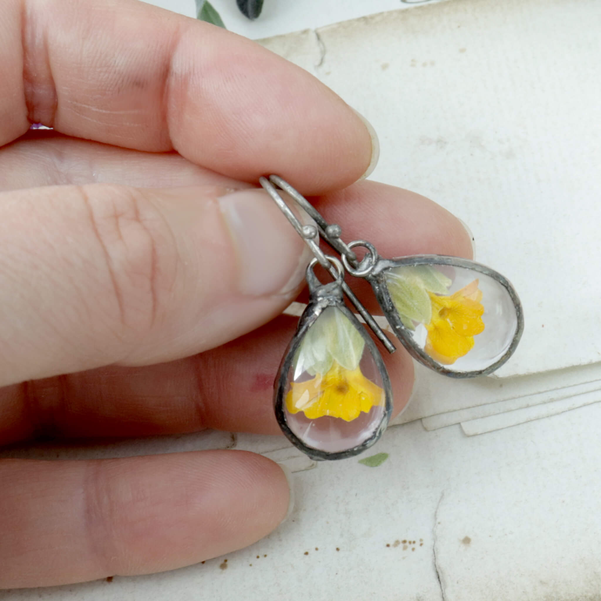 Hand holding primroses in soldered glass earrings
