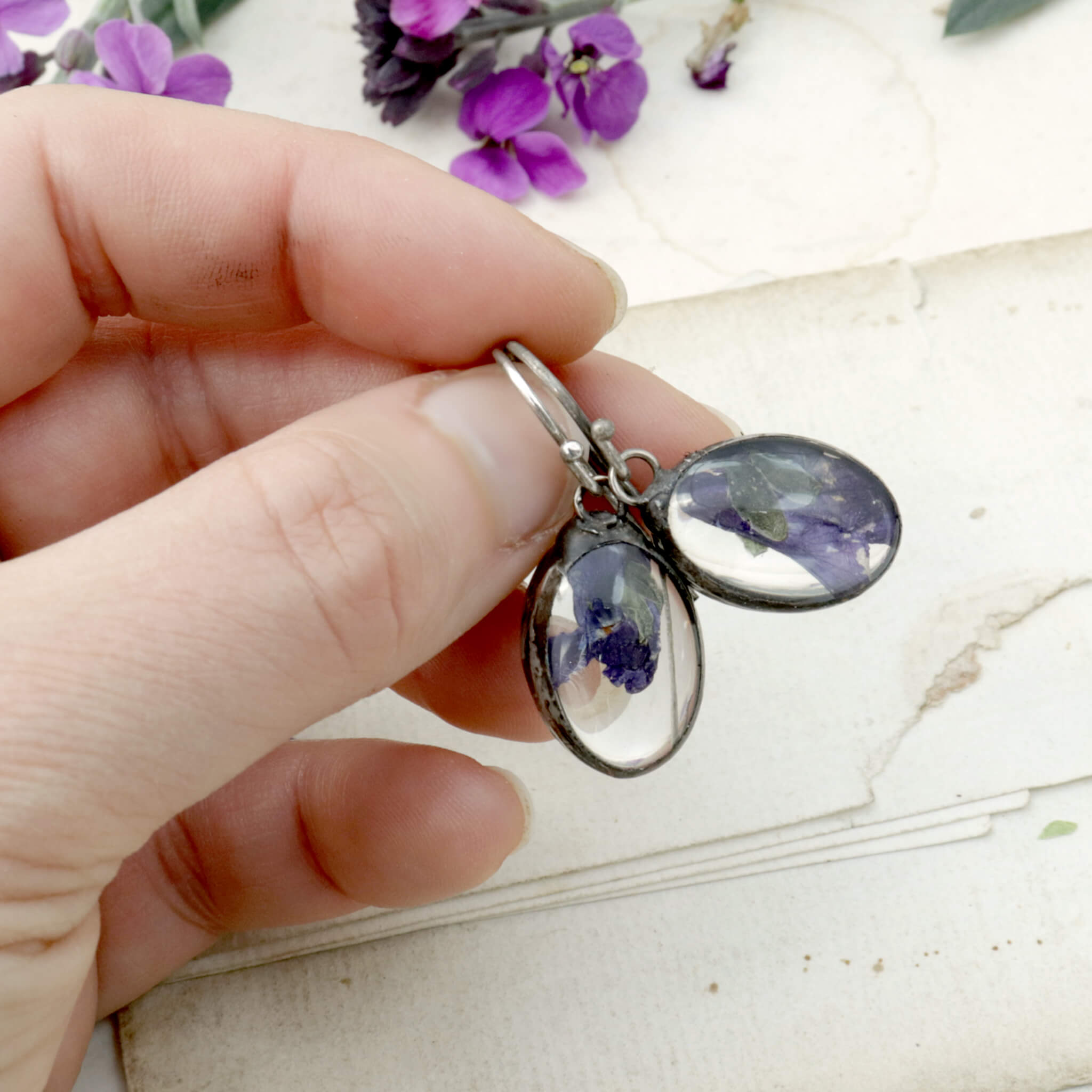 Earrings with real sweet violet flowers being hold in hand