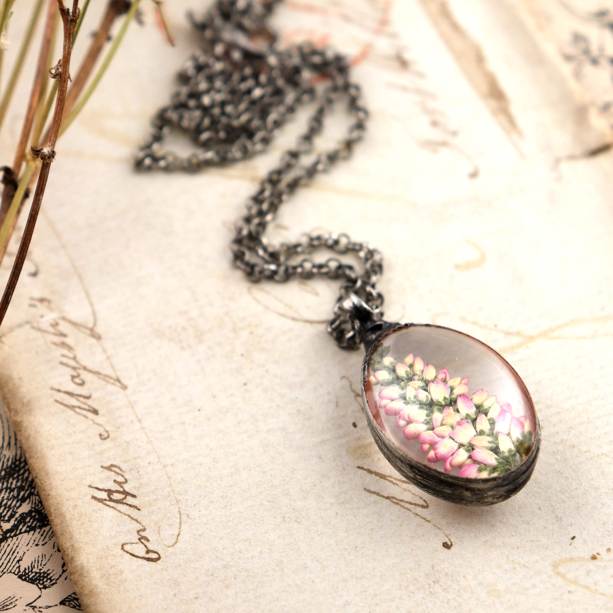 Pressed heather in a stained glass necklace lying on a vintage letter