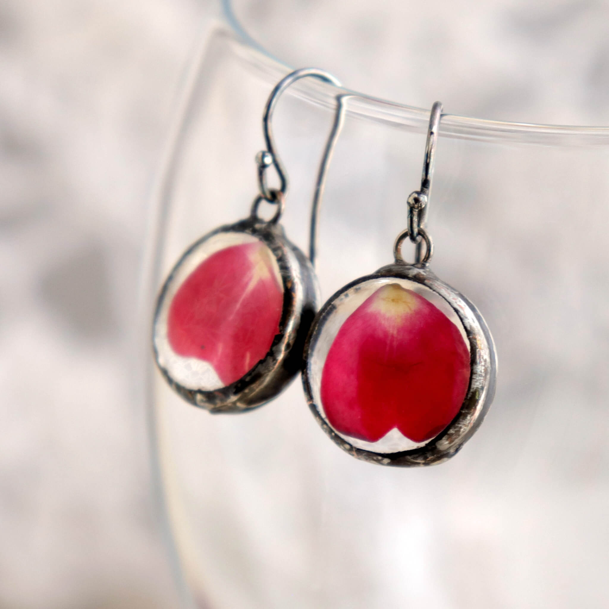 Rose petal earrings hanging from the edge of a wine glass