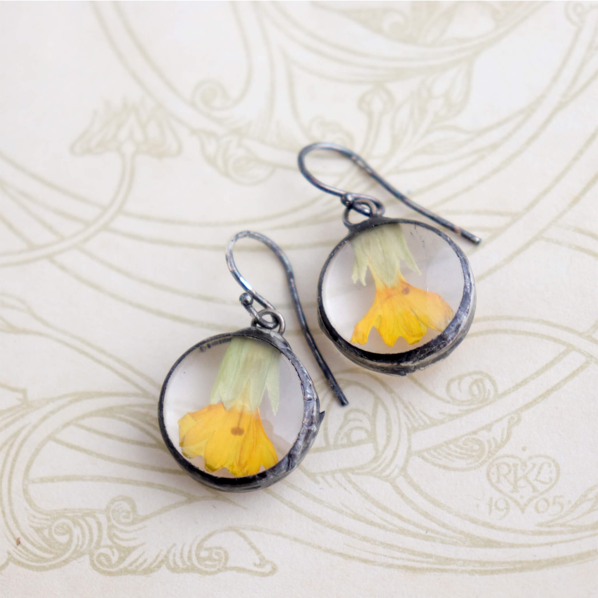 Round earrings with yellow flowers inside lying on an old book