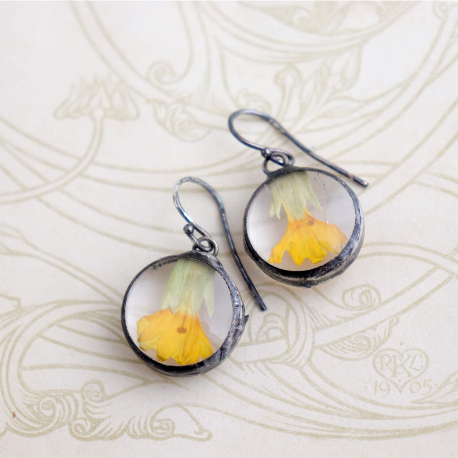 Primroses in soldered glass earrings hanging from the edge of a glass