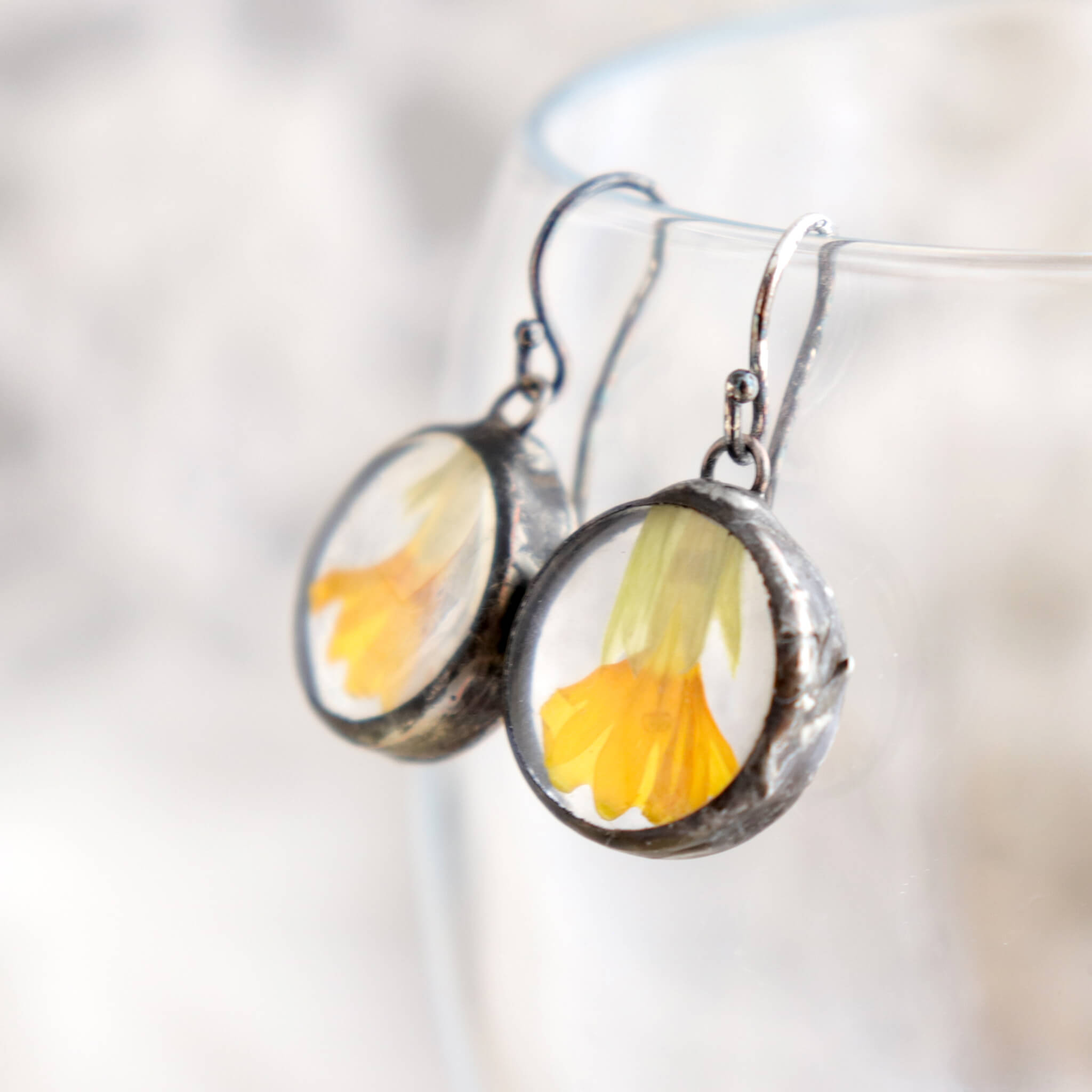 Primroses in soldered glass earrings hanging from the edge of a glass