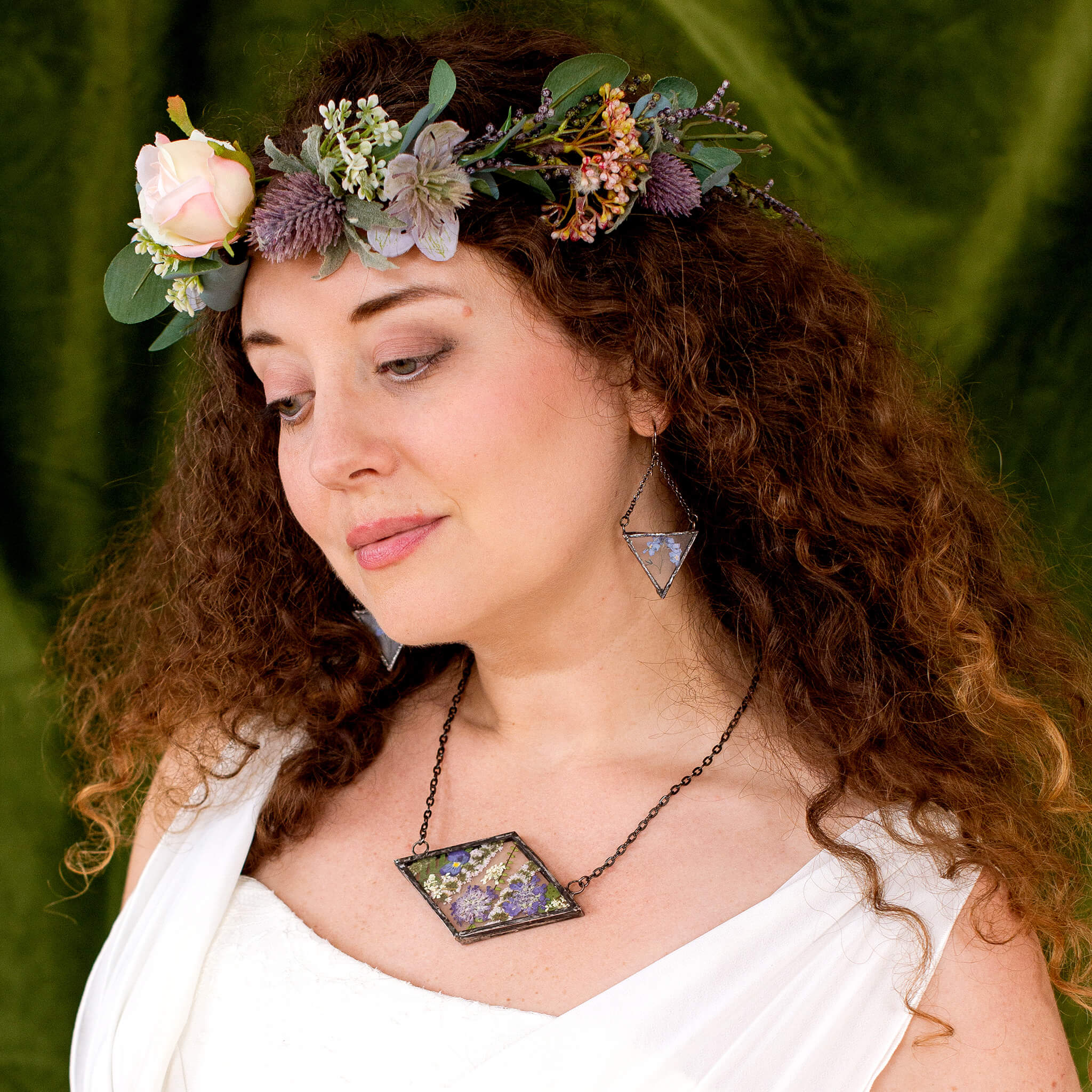 Brunette in white dress and flower crown wearing rhomboidal Purple pressed flower necklace