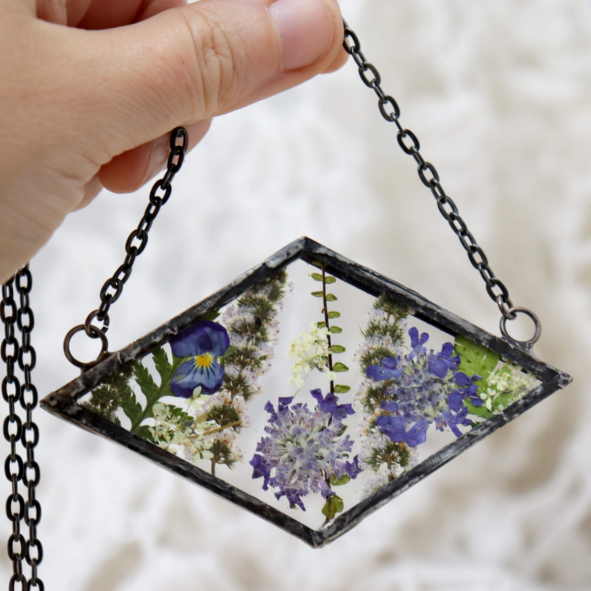 Hand holding Rhomboidal purple pressed flower necklace