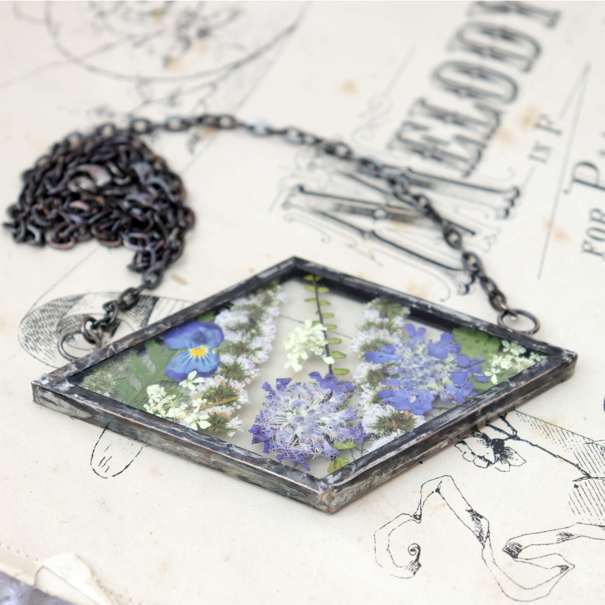 Rhomboidal purple pressed flower necklace lying on an old book
