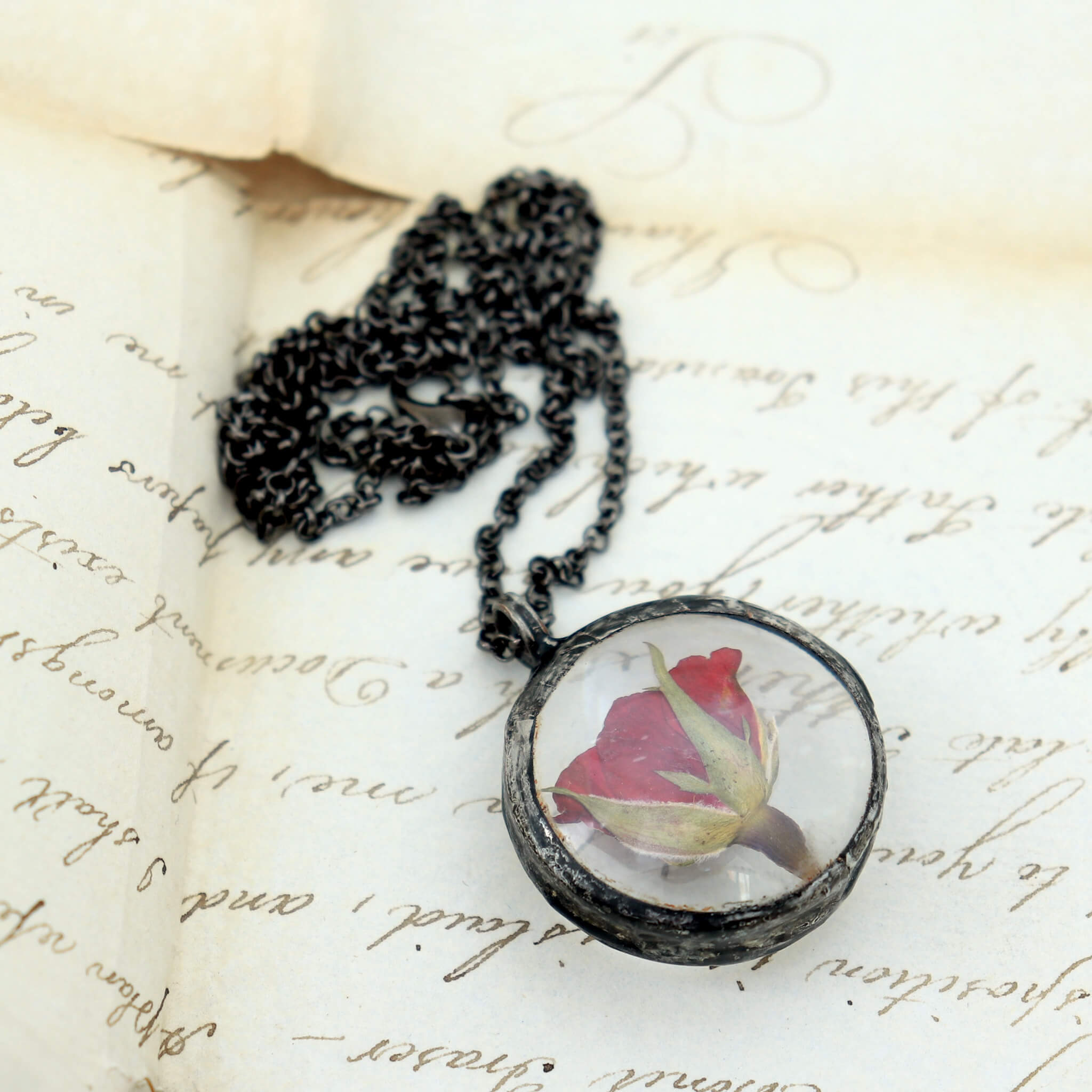 pressed rose pendant necklace lying on an old letter