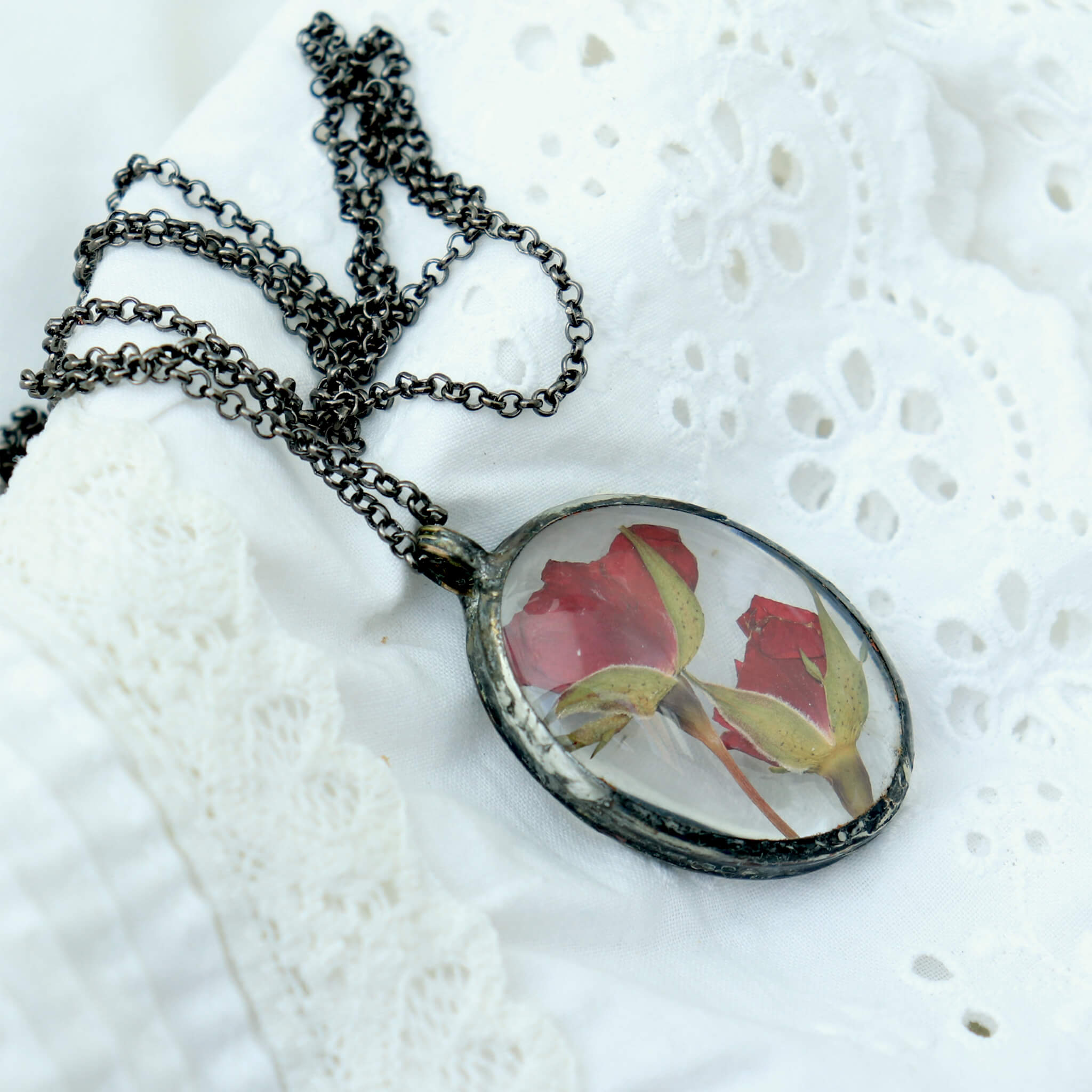 Pressed rose in soldered glass pendant necklace lying on white lace