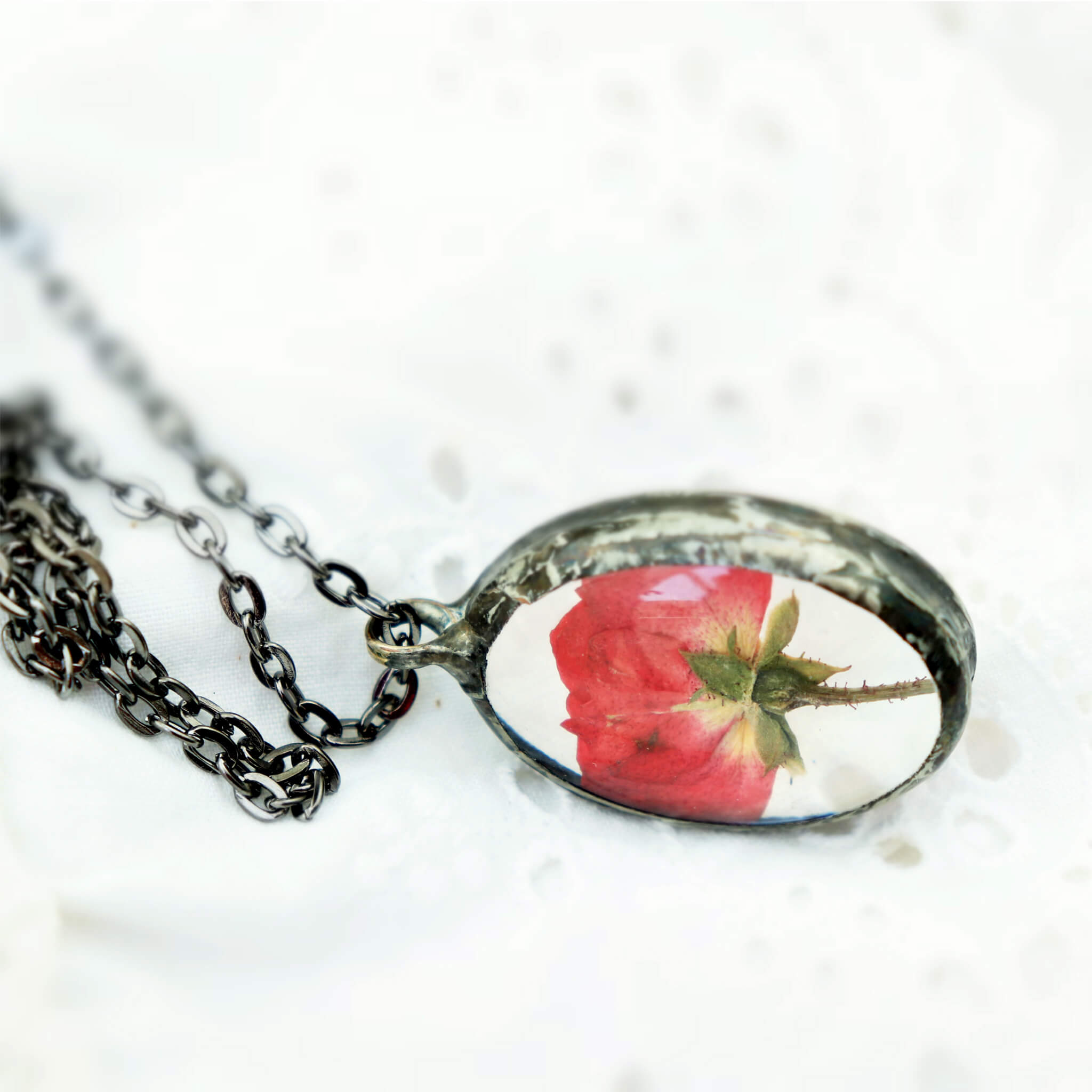 Pressed rose in soldered glass pendant necklace lying on white lace