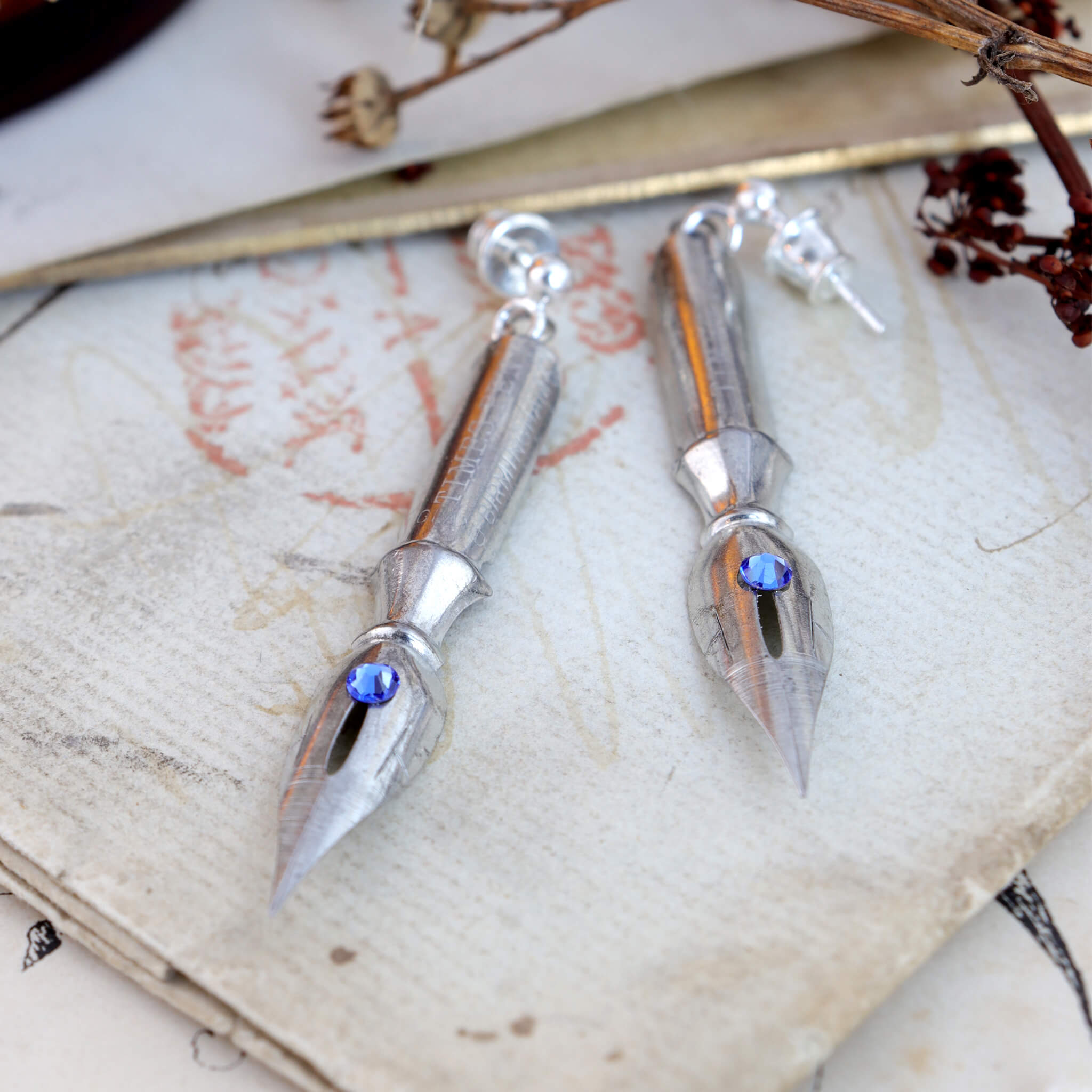 pen nib earrings with sapphire birthstone crystals on them lying on vintage paper