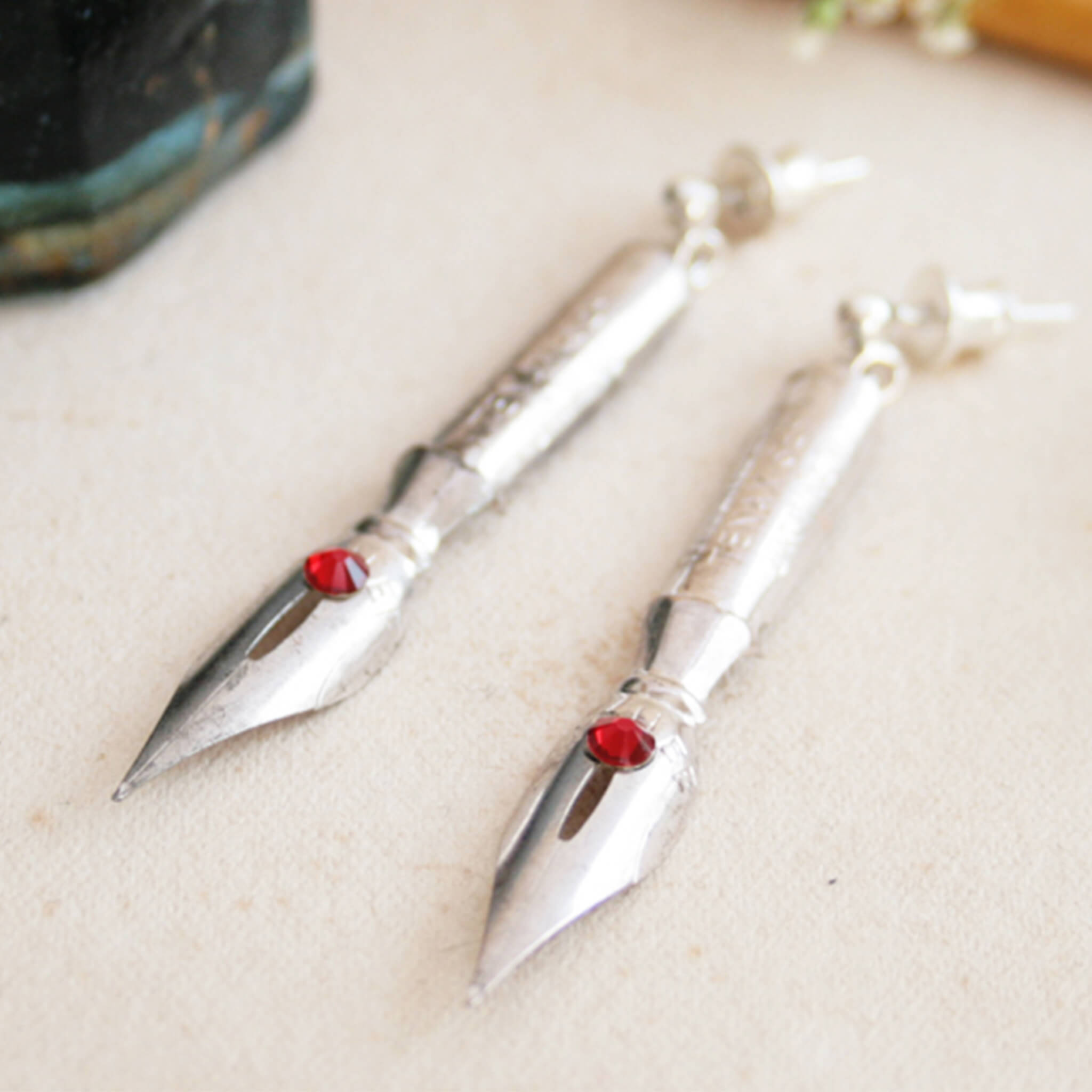 pen nib earrings with siam birthstone crystals on them lying on vintage paper