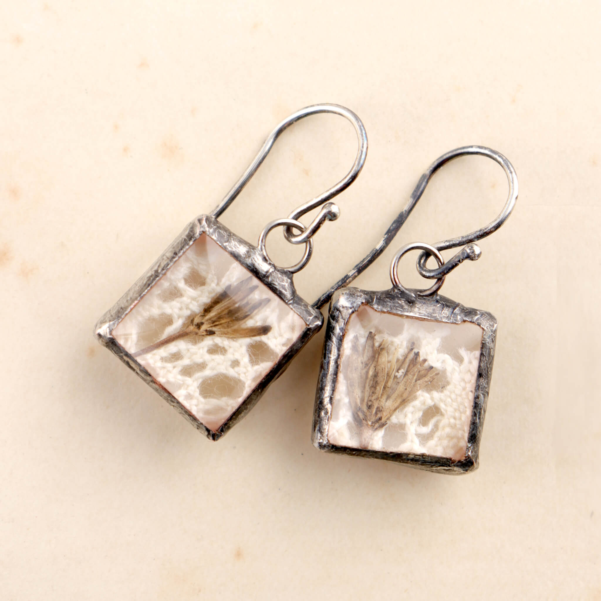 Square soldered earrings with vintage lase and pressed flowers lying on an old letter