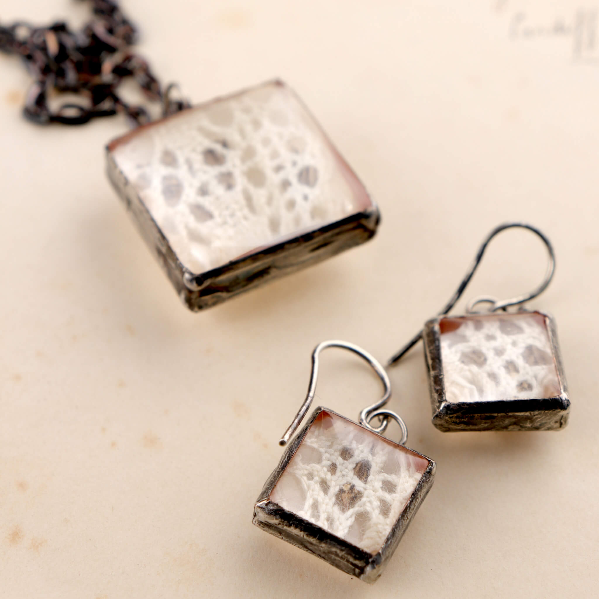 Square soldered jewellery set with vintage lase and pressed flowers lying on an old letter