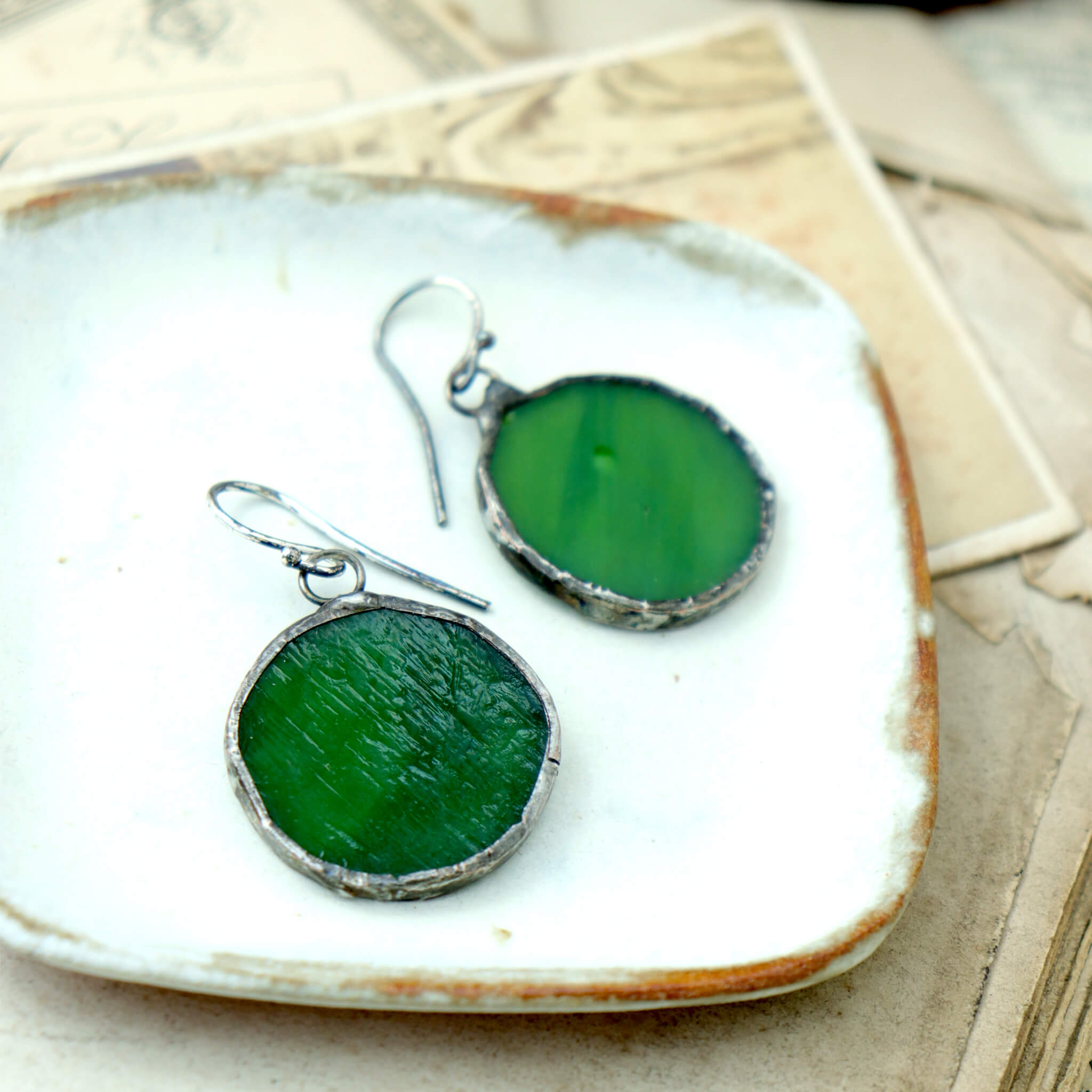 circles of glass in green colour turned into stained glass earrings lying on a white dish