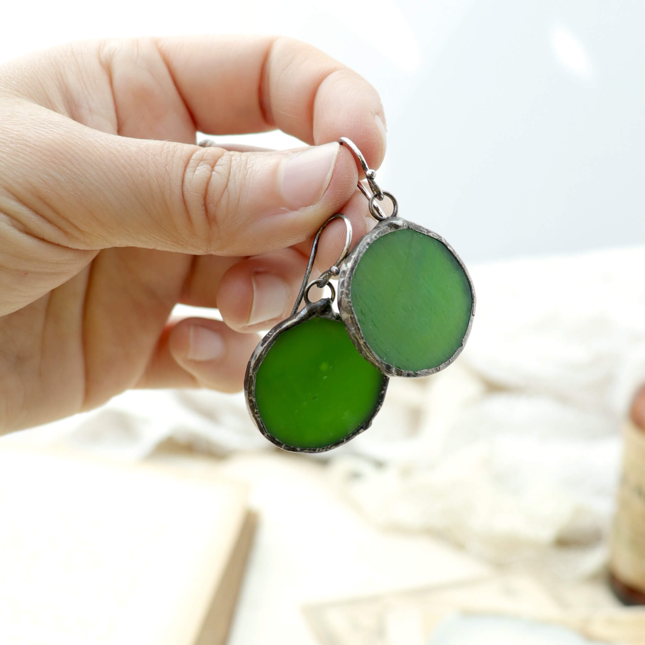 hand holding circles of glass in green colour turned into stained glass earrings