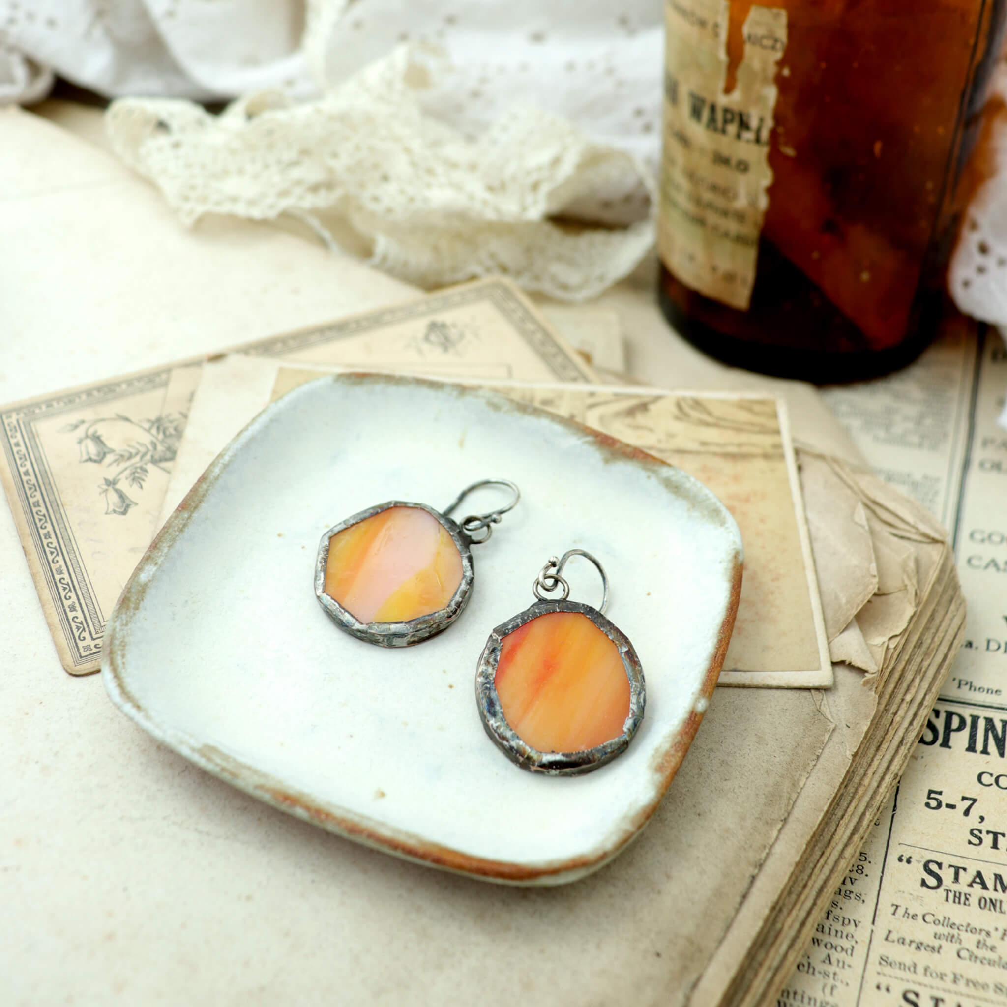 circles of glass in orange colour turned into stained glass earrings lying on a white dish