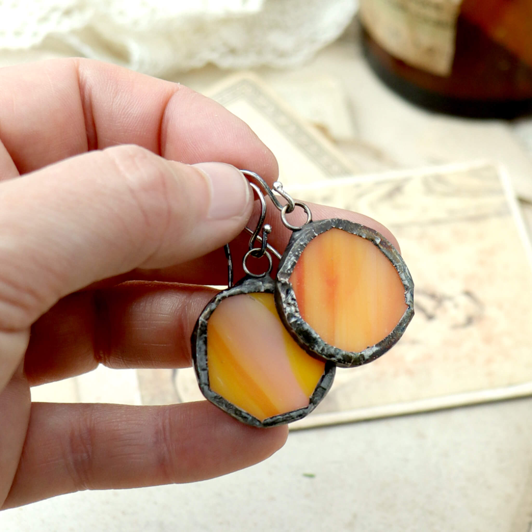 hand holding circles of glass in orange colour turned into stained glass earrings