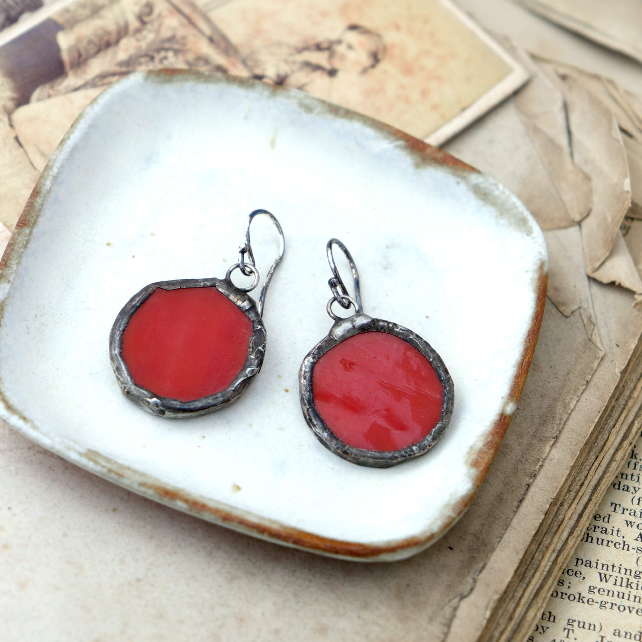 circles of glass in red colour turned into stained glass earrings lying on a white dish
