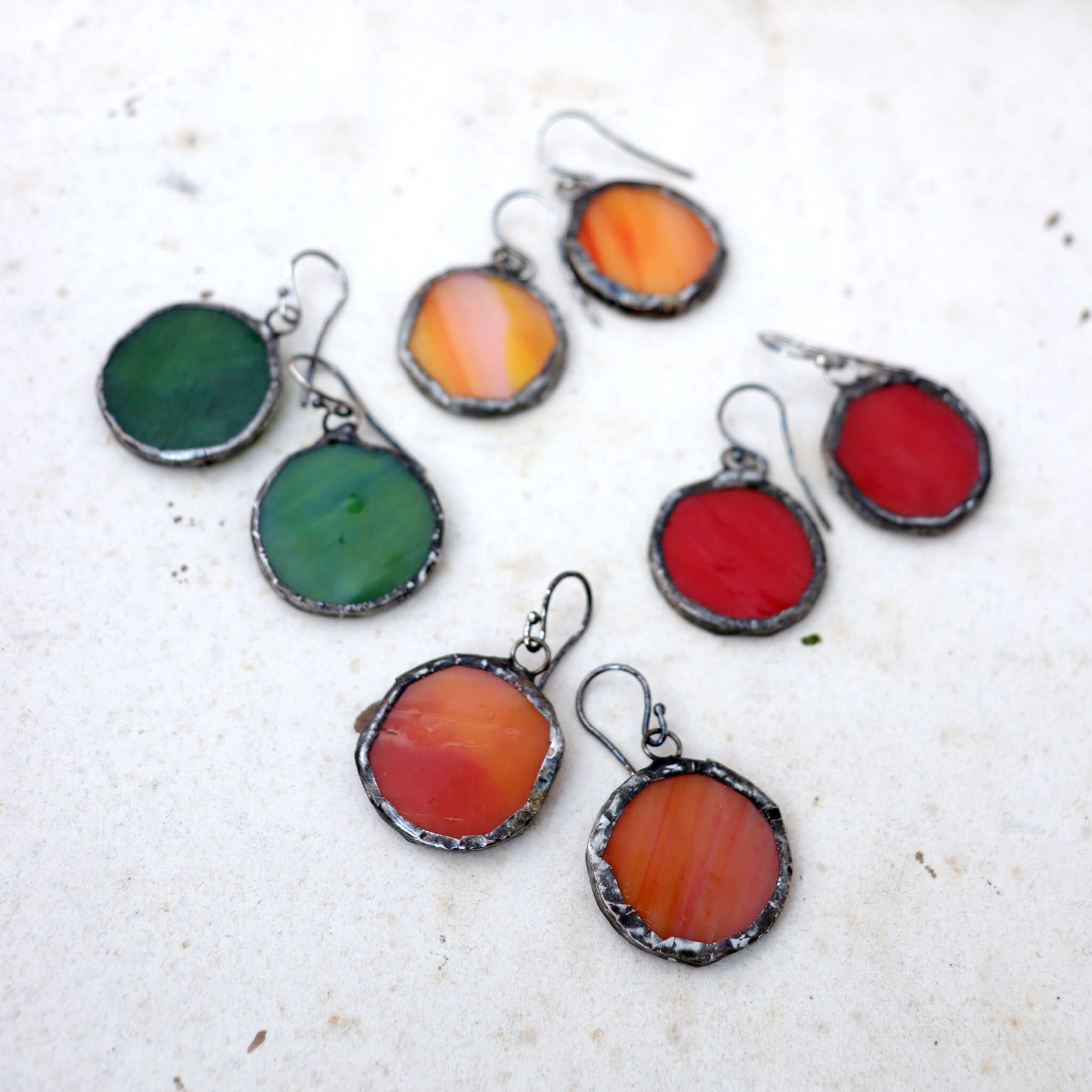 circles of glass in green, red and orange colour turned into stained glass earrings on a paper