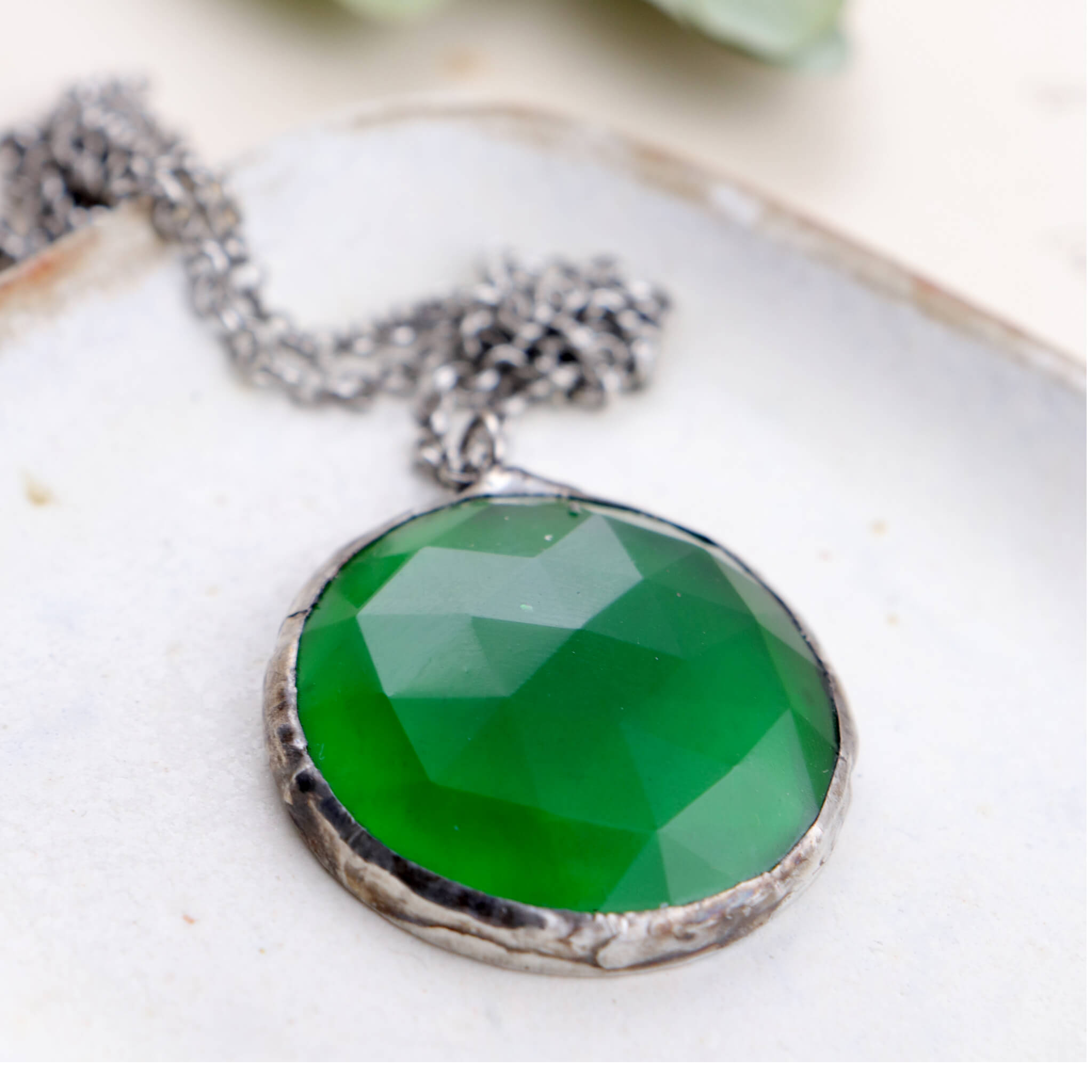 Faceted emerald glass framed into necklace lying on a dish