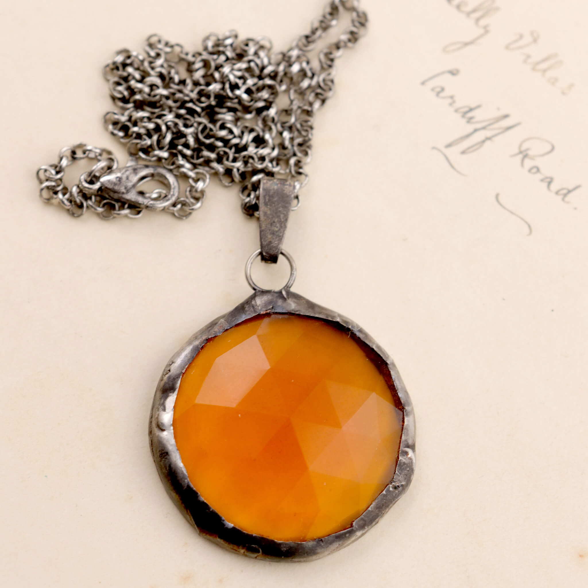 Faceted amber glass framed into necklace lying on an old letter