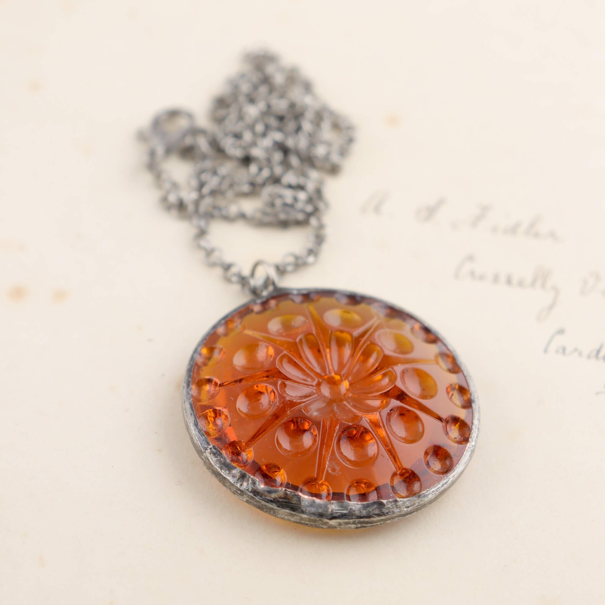 Centric pattern amber glass rondelle framed into stained glass necklace lying on an old letter
